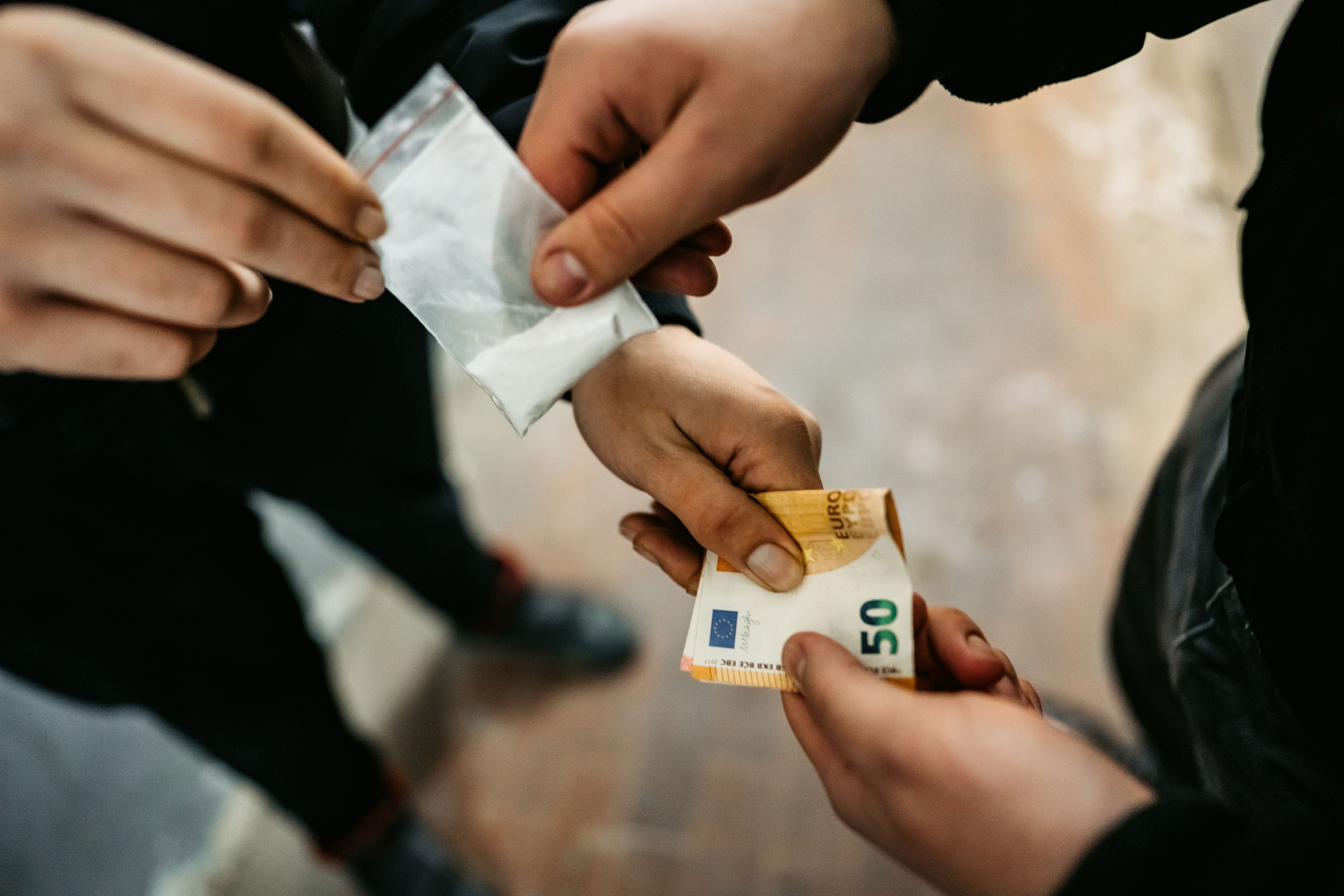 Nahaufnahme eines Austauschs von Geldscheinen gegen ein Tütchen mit weißem Pulver zwischen zwei Personen.