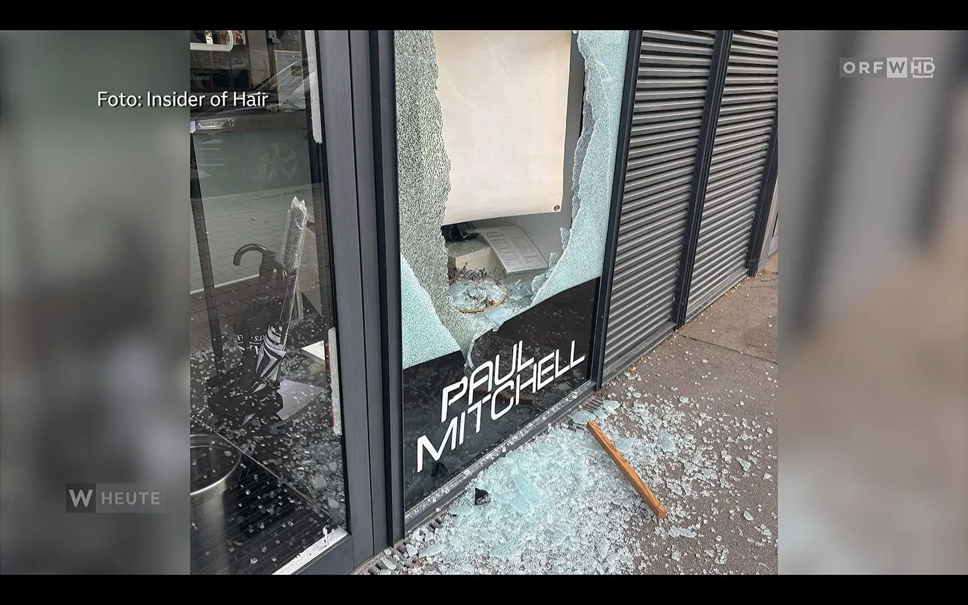 Zerbrochene Schaufensterscheibe eines Paul Mitchell Friseursalons mit Glasscherben auf dem Boden.