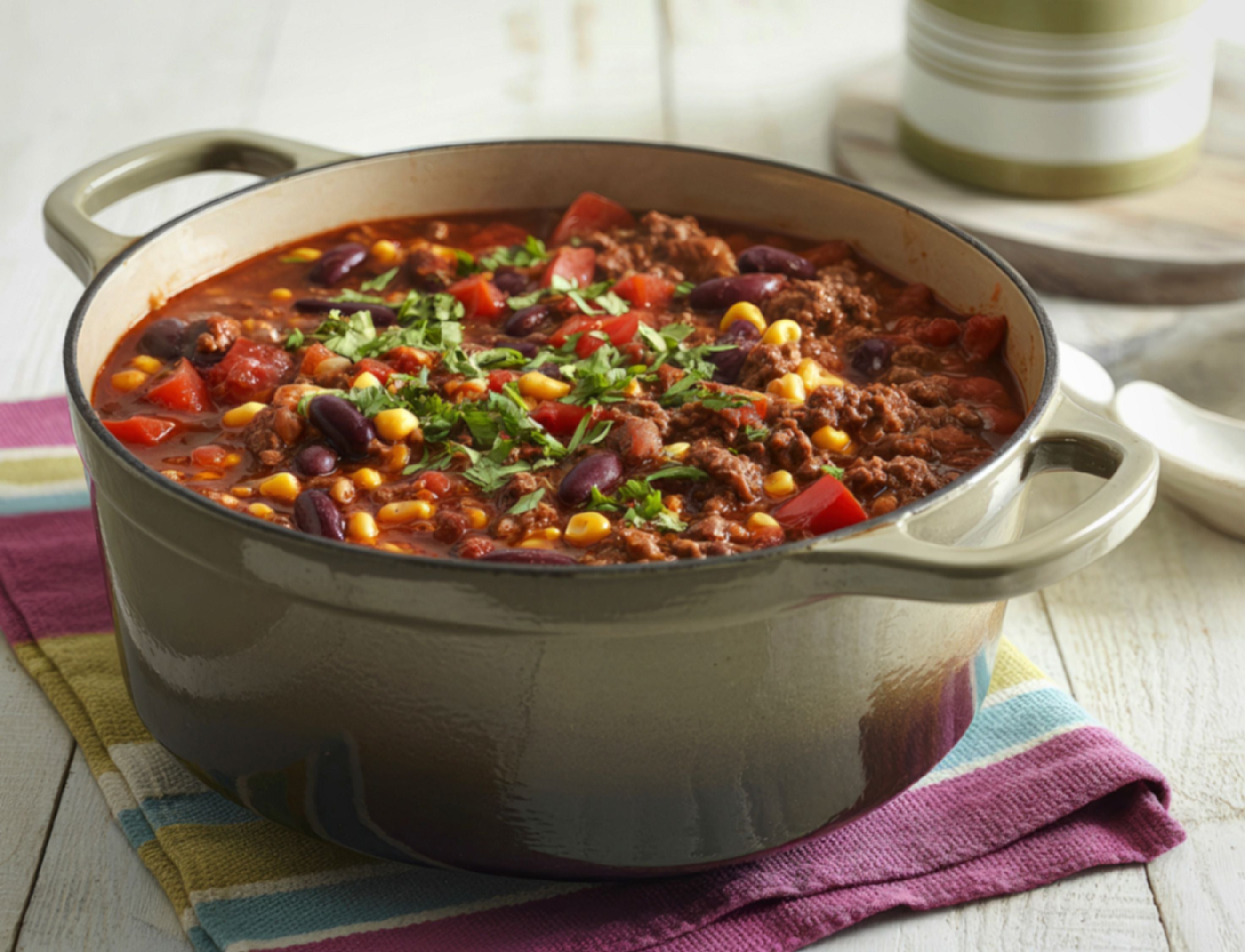 Ein Topf mit Chili con Carne, garniert mit frischen Kräutern, steht auf einem bunten Tuch.
