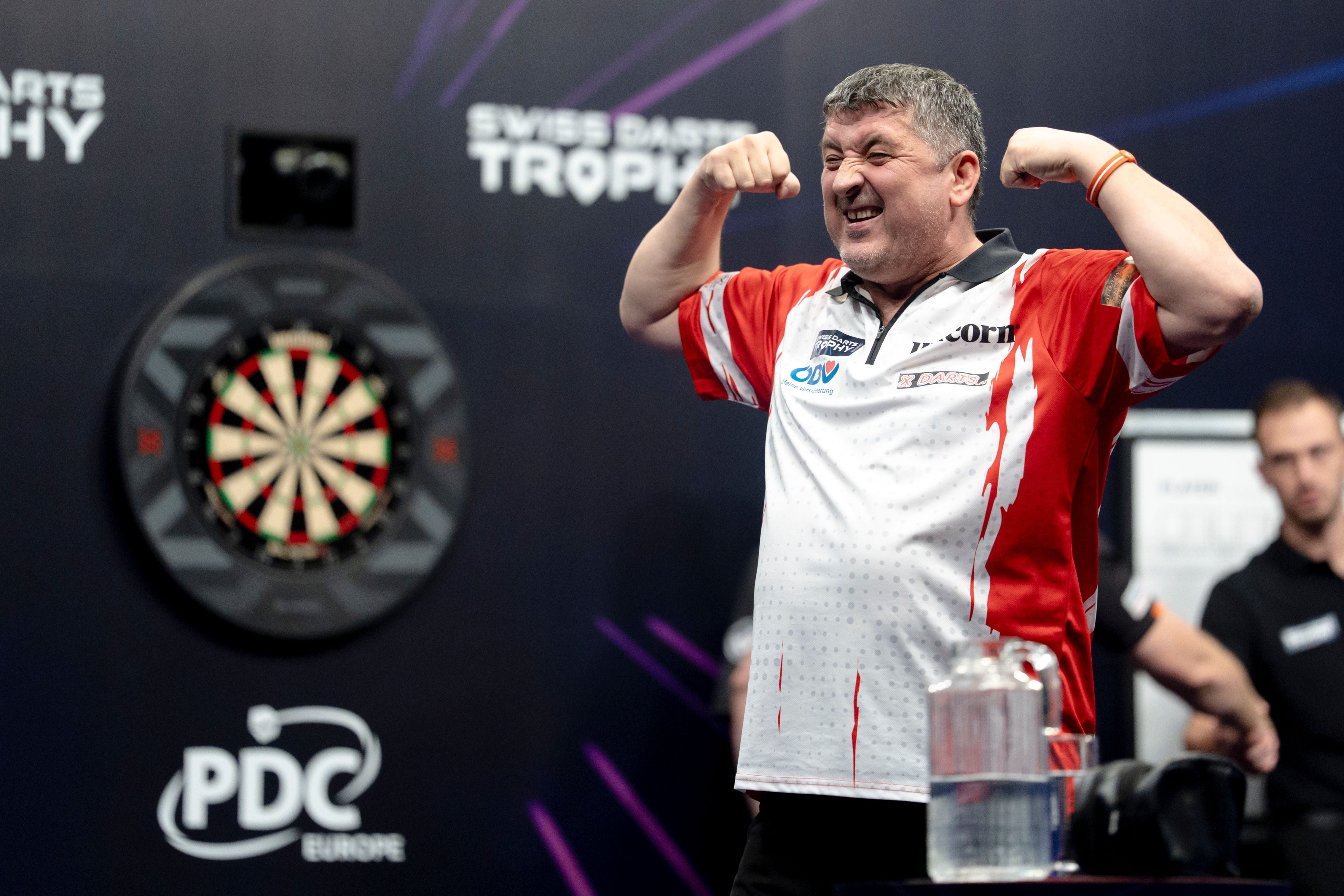 Ein Dartspieler jubelt mit geballten Armen auf einer Bühne vor einer Dartscheibe.