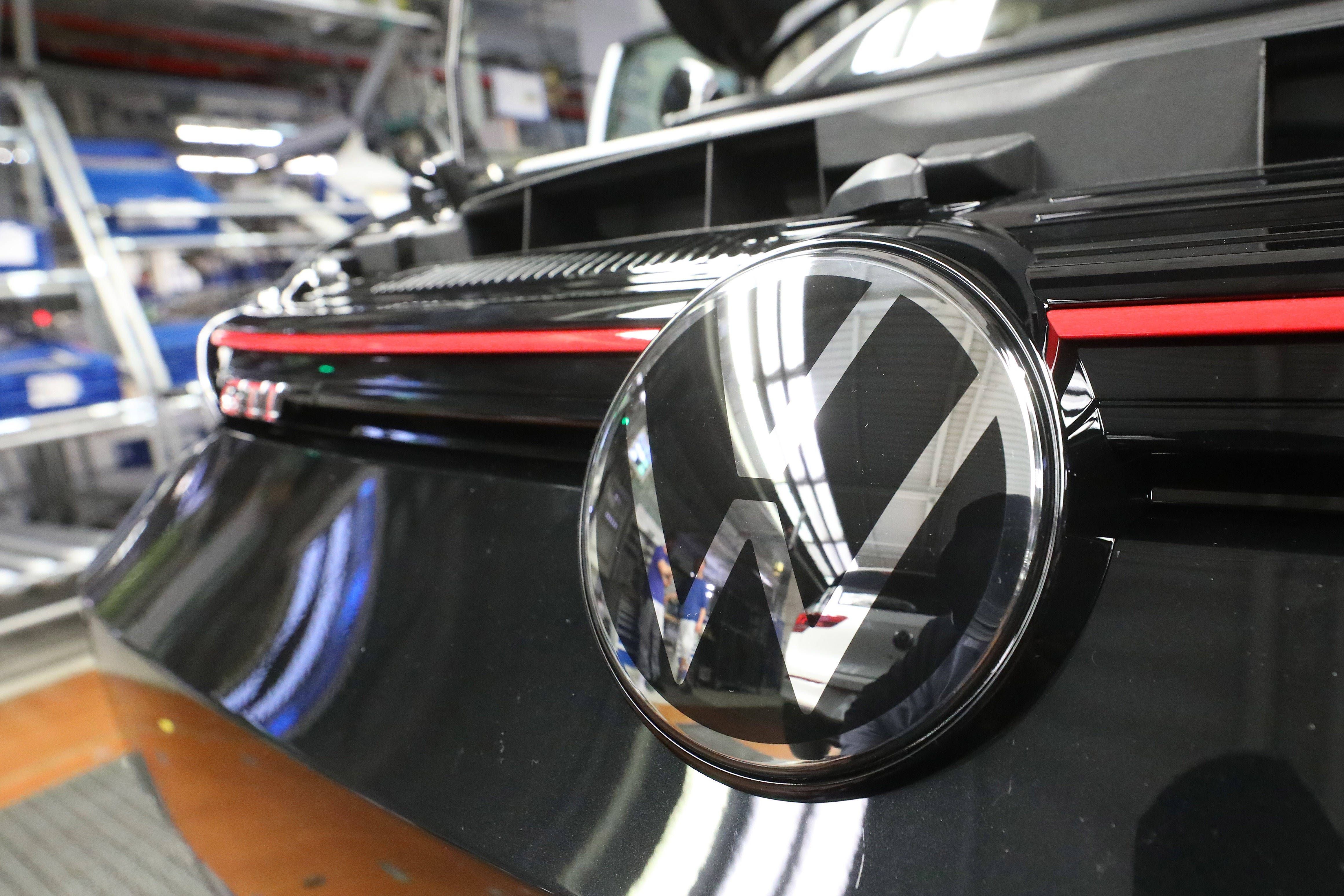 Nahaufnahme des VW-Logos an einem schwarzen VW Golf 8 GTI in der Produktionshalle.