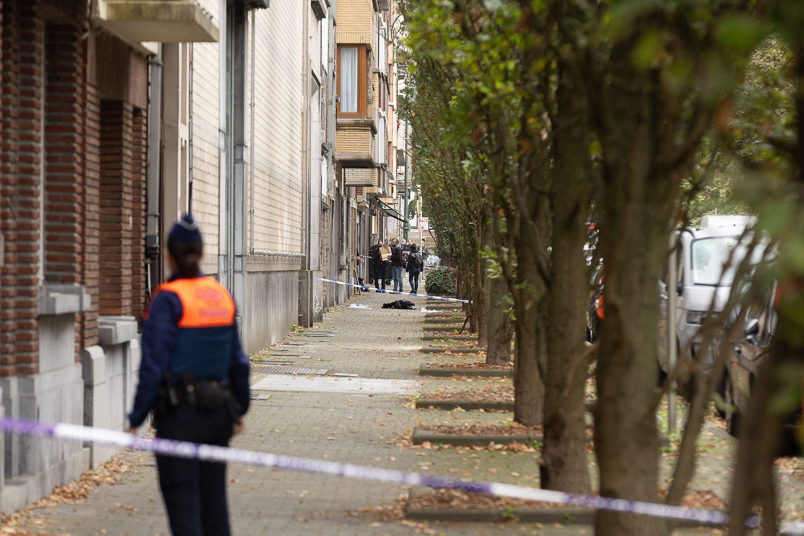 Polizeibeamte sichern nach einer Schießerei eine abgesperrte Straße in Brüssel, Bäume am Gehweg.