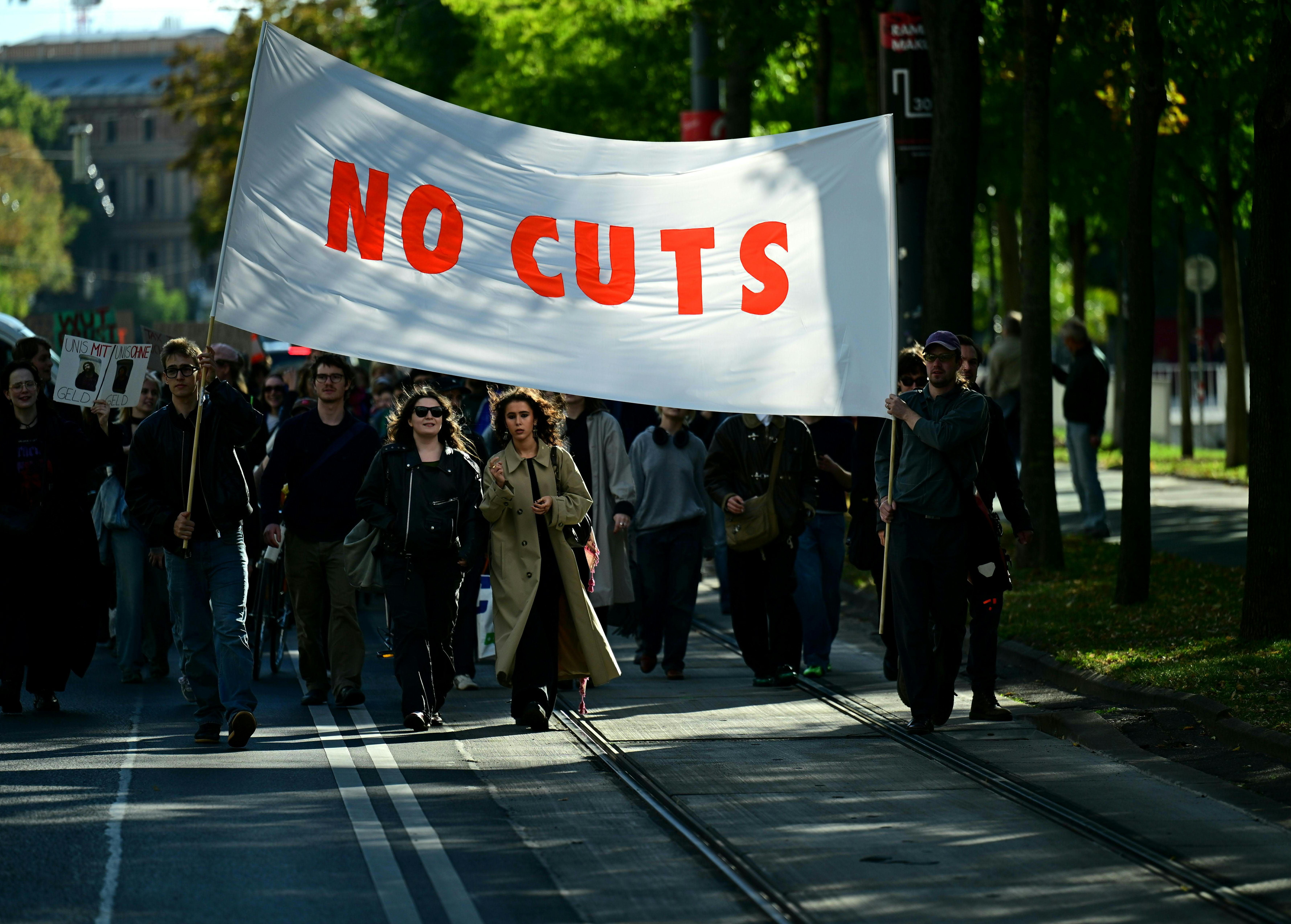 Mehrere Menschen tragen ein Banner mit der Aufschrift "NO CUTS" bei einer Demonstration in Wien.