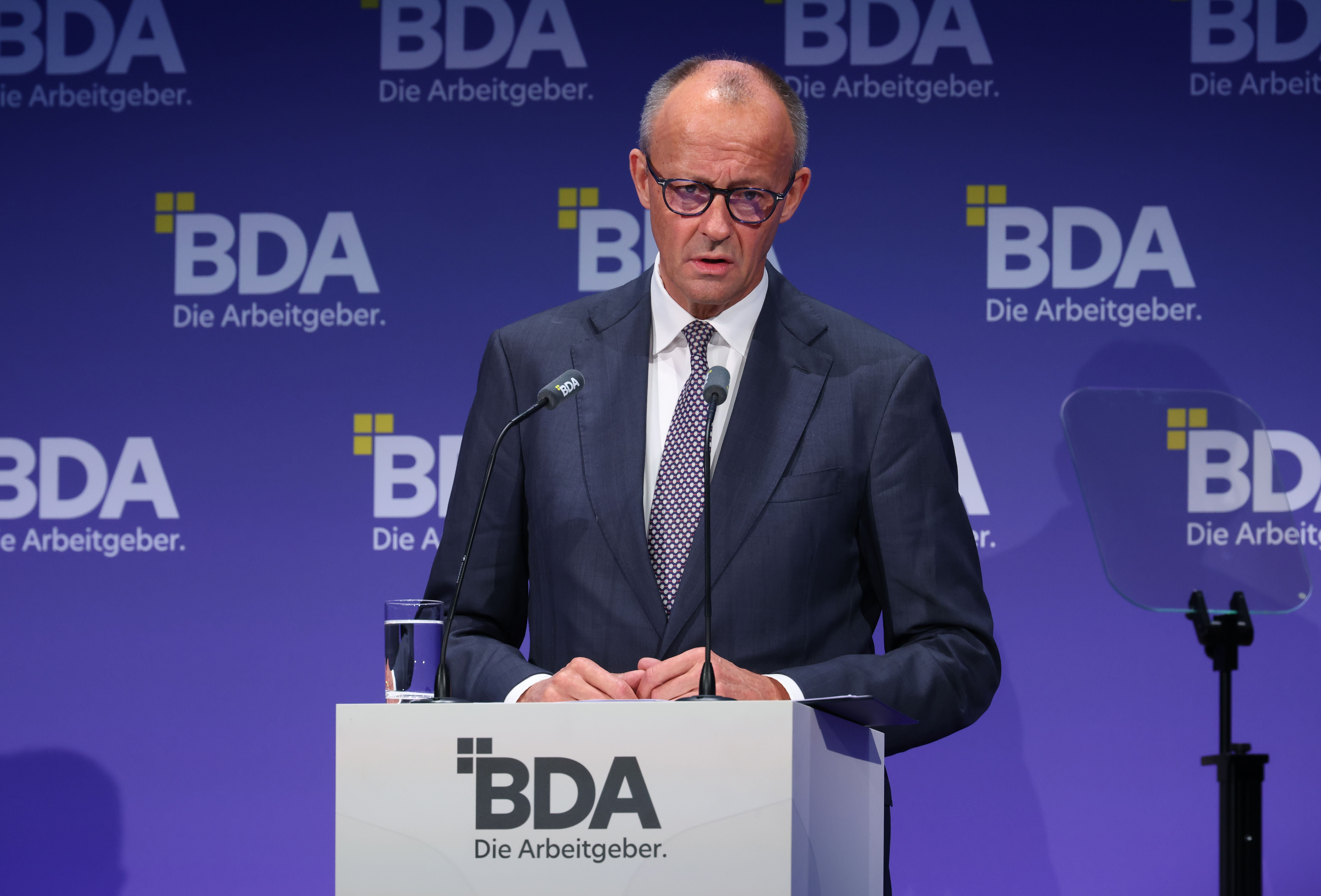Ein Mann im Anzug spricht am Rednerpult auf dem BDA-Kongress vor lila Hintergrund.