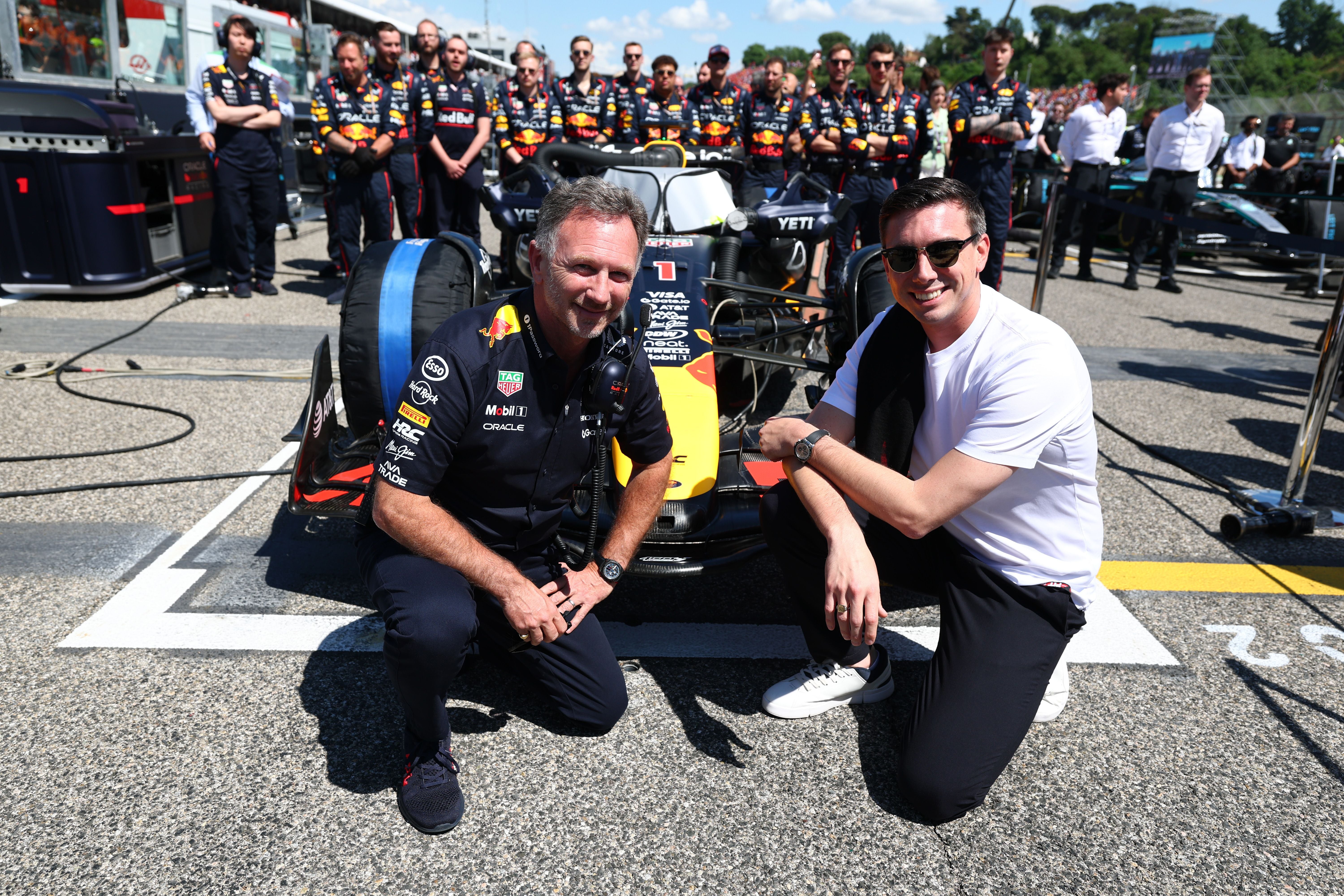 Zwei Männer knien vor einem Red Bull Formel-1-Auto auf der Startaufstellung in Imola.