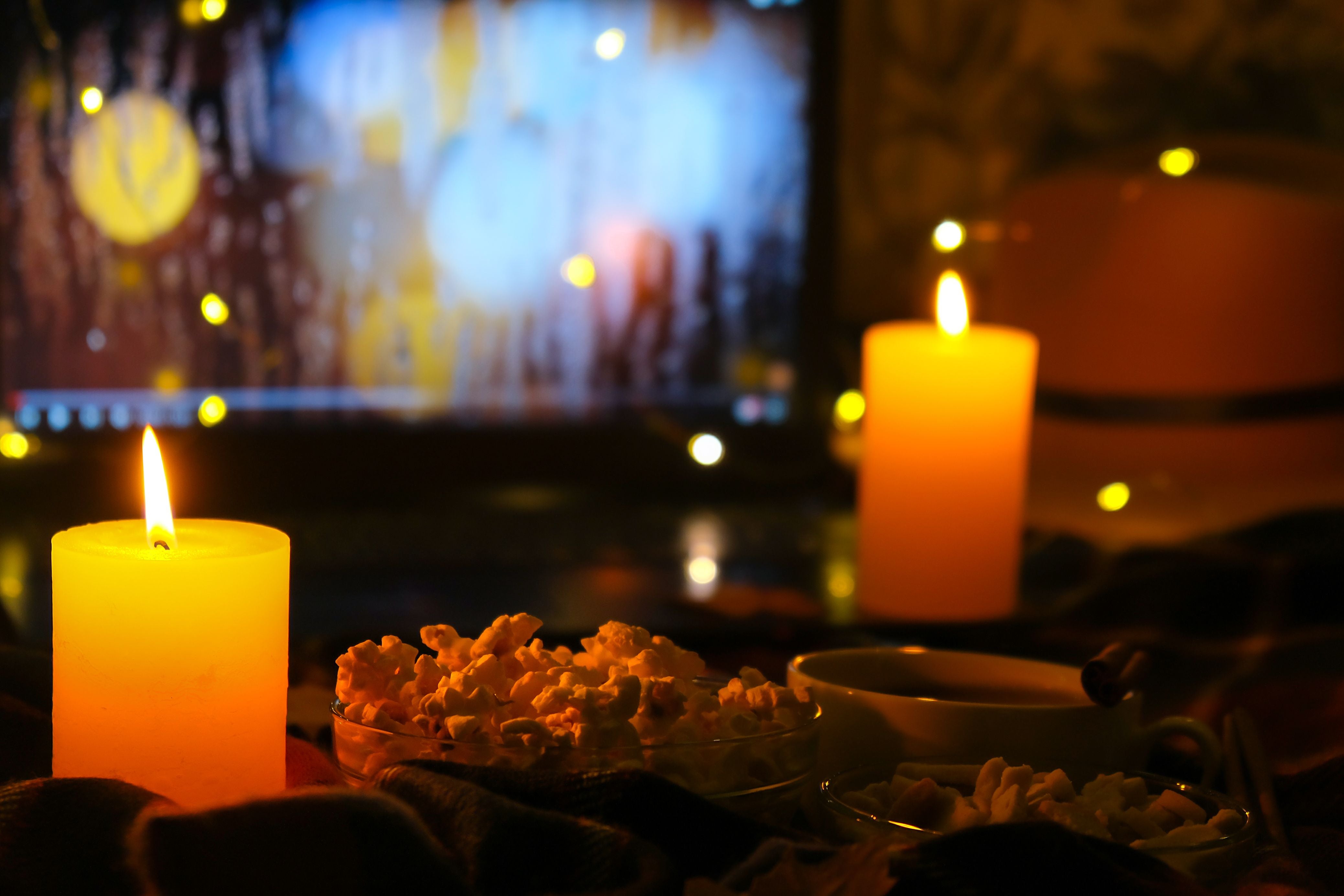 Gemütliche Szene mit Kerzenlicht, Popcorn und Laptop im Hintergrund, herbstliche Stimmung im Zimmer.