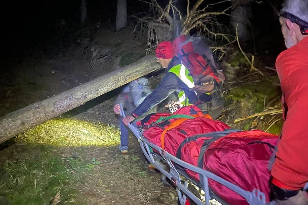 Rettungskräfte transportieren nachts eine verletzte Person auf einer Trage durch den Wald.