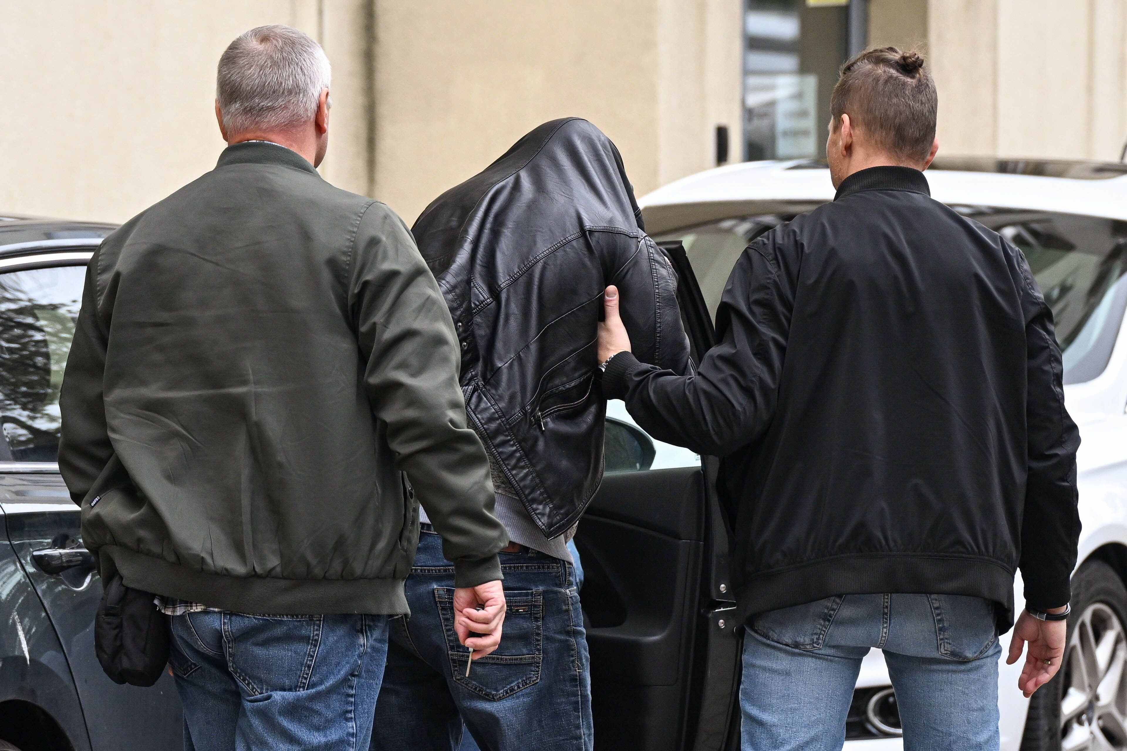 Zwei Polizisten führen einen Mann mit verhülltem Kopf zu einem Gebäude.