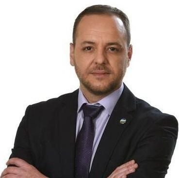 Ein Mann im Anzug mit verschränkten Armen vor weißem Hintergrund.