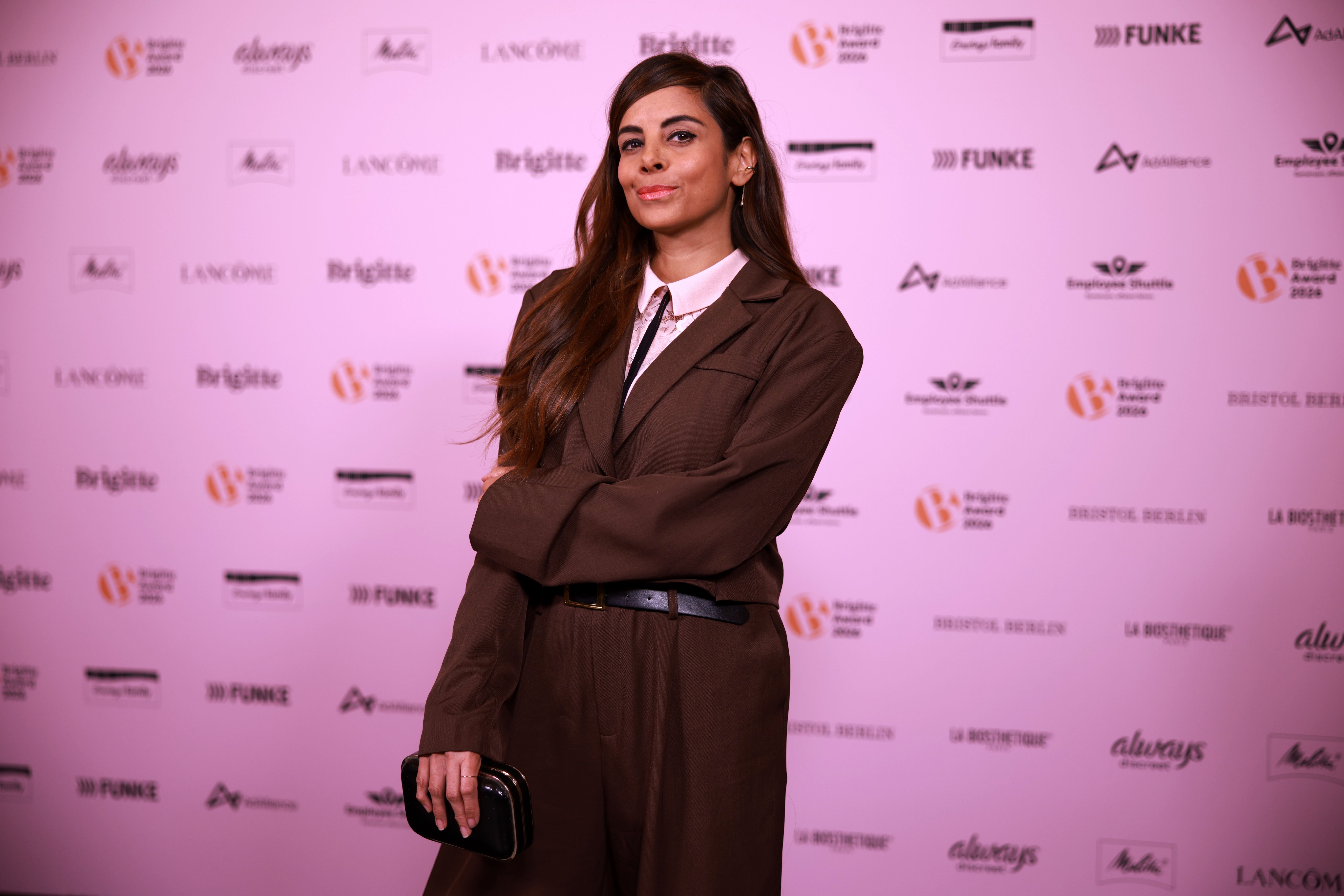 Eine Frau in braunem Anzug posiert vor einer Fotowand beim Brigitte Magazin Award.