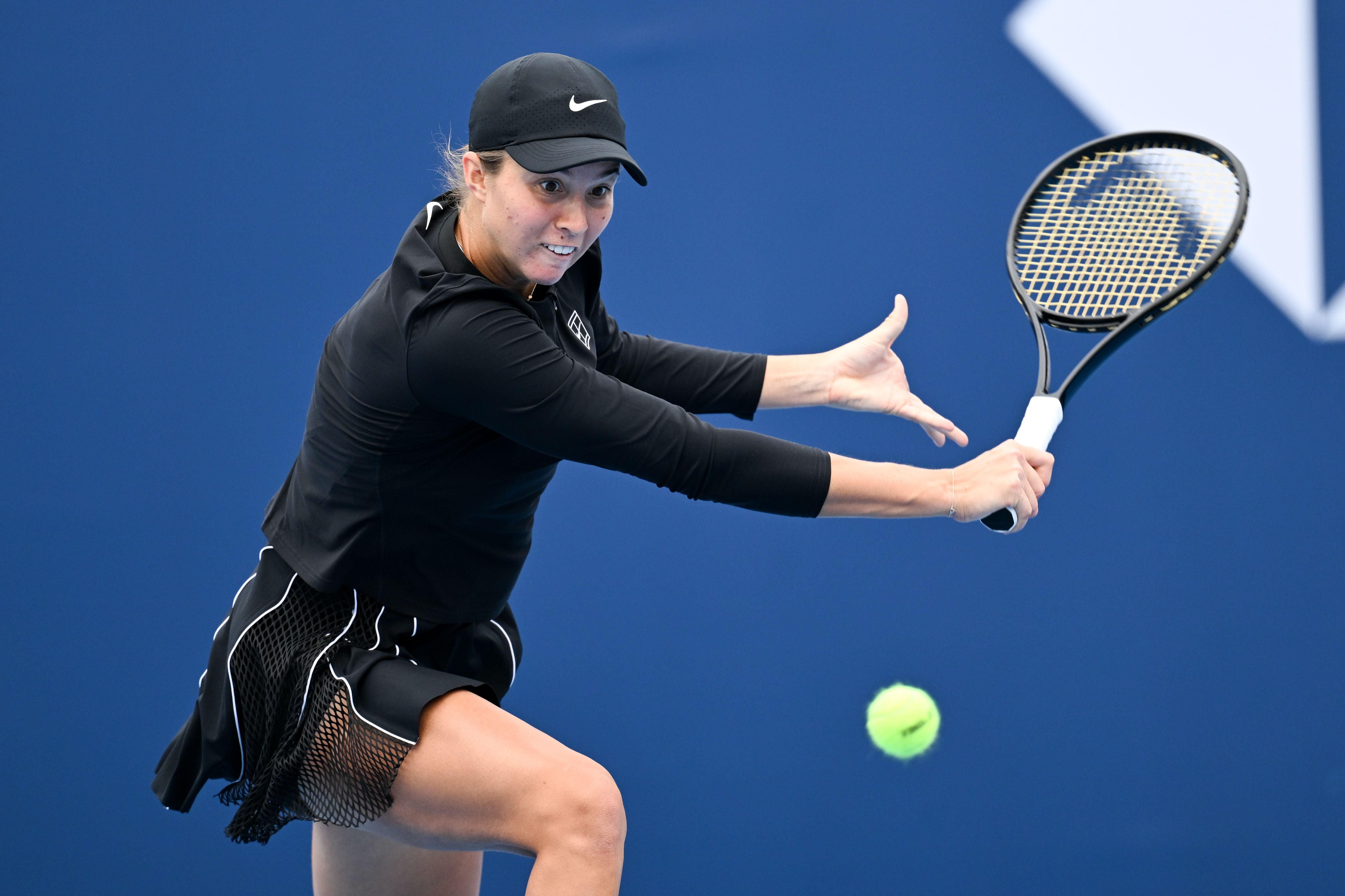 Eine Tennisspielerin schlägt eine Rückhand auf einem blauen Tennisplatz.