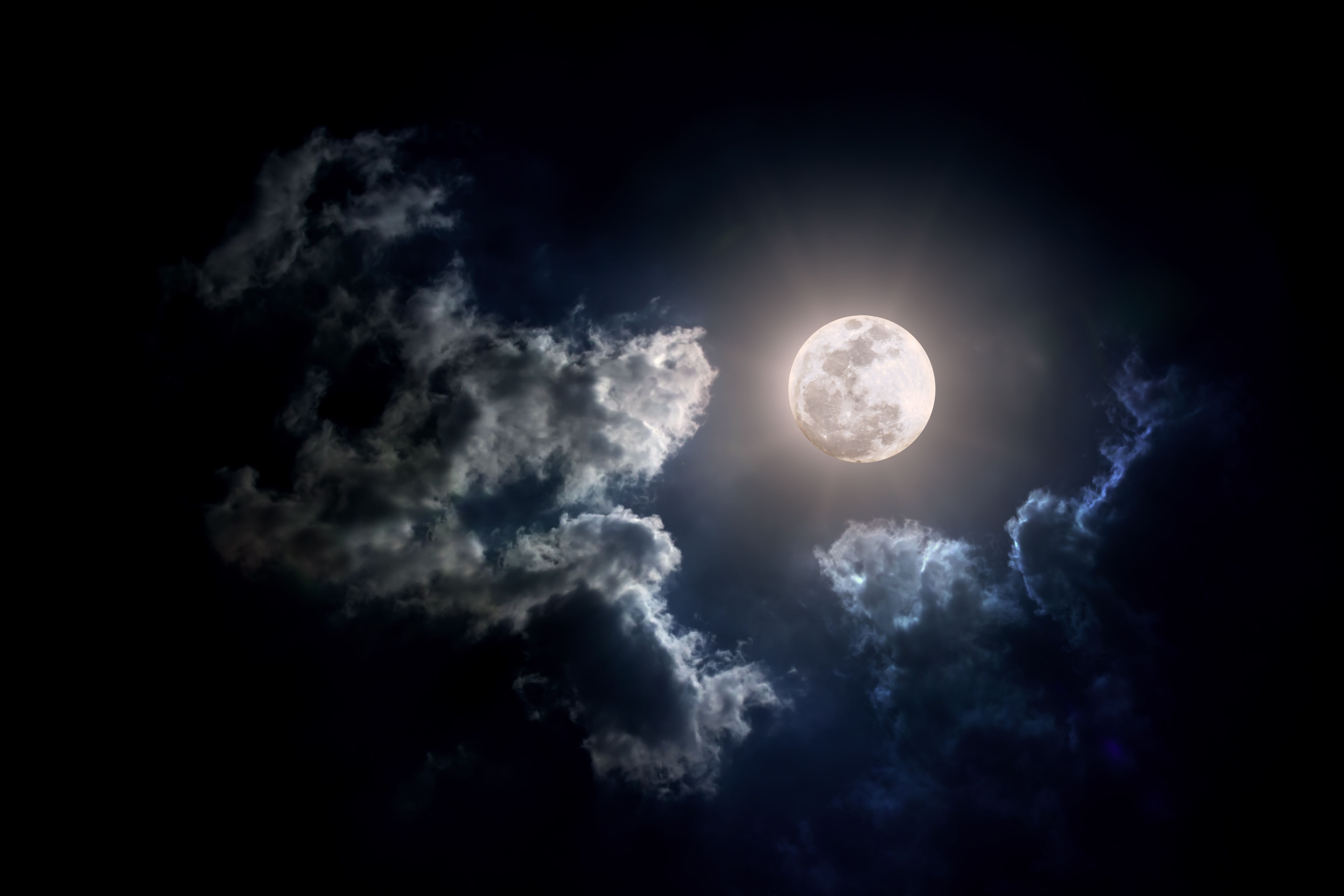 Vollmond leuchtet hell am Nachthimmel, umgeben von dunklen, teils beleuchteten Wolken.