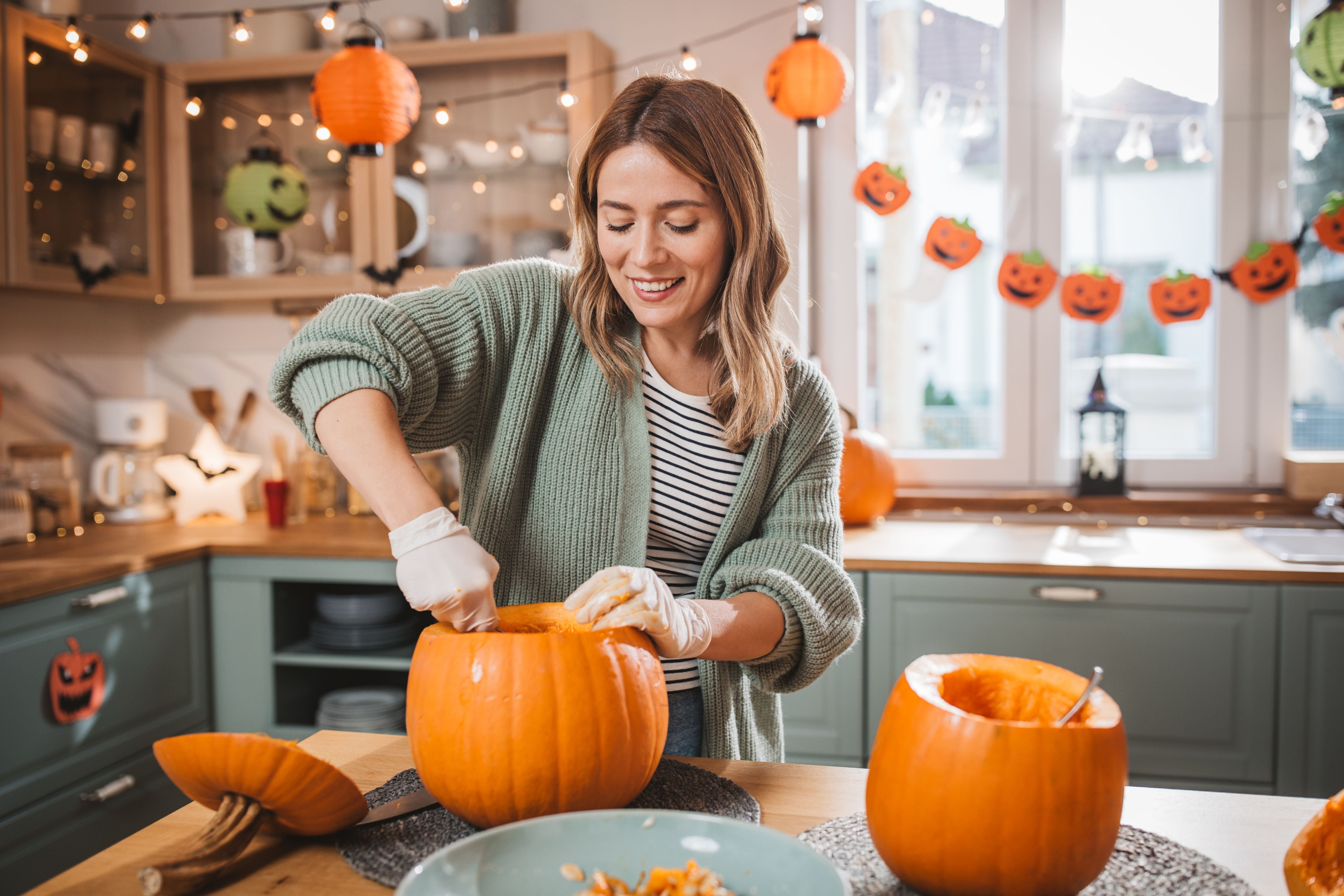 Junge Frau höhlt einen Kürbis für Halloween in einer festlich dekorierten Küche aus.
