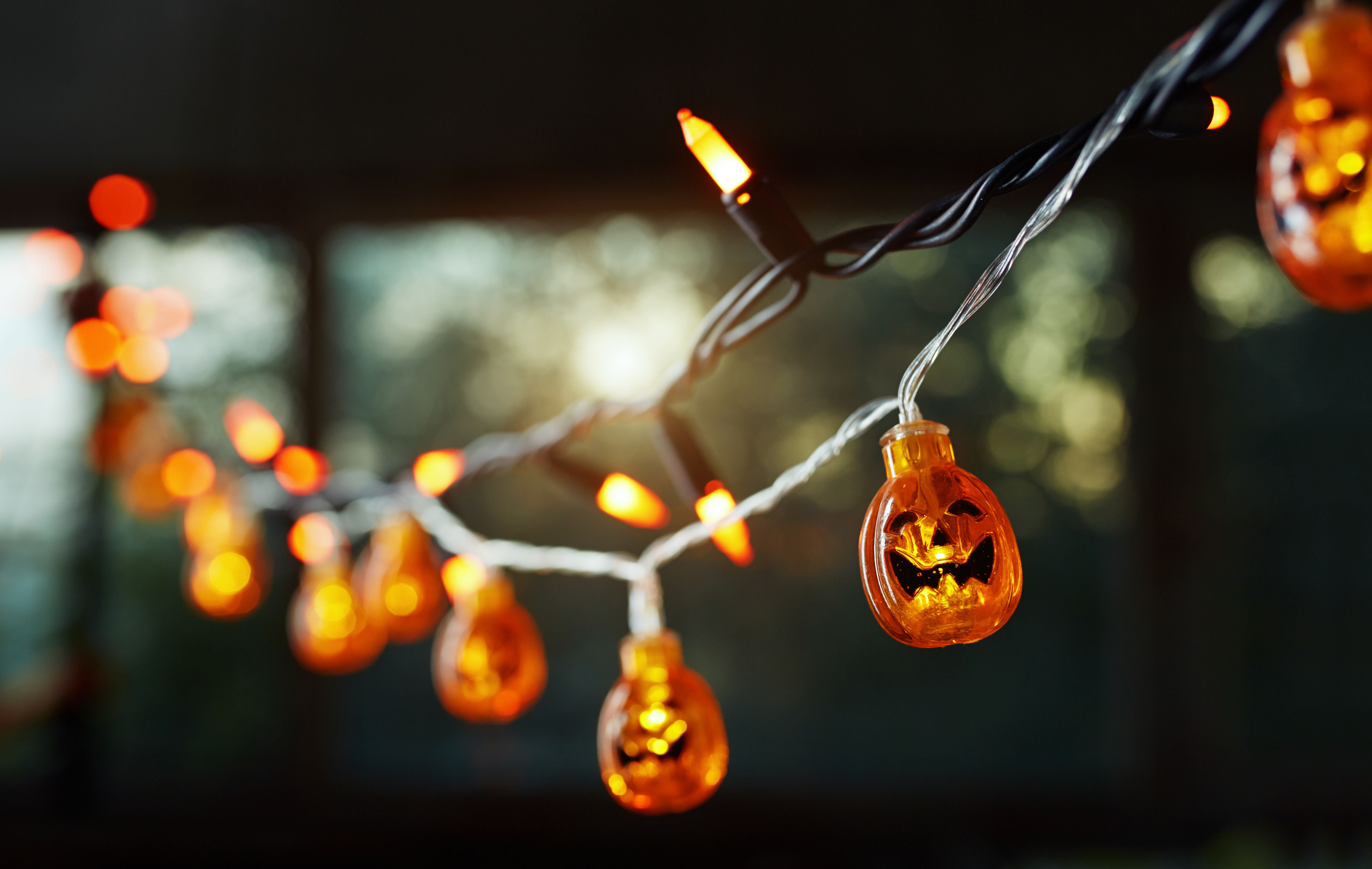Lichterkette mit leuchtenden Kürbissen als Halloween-Deko vor einem Fenster im Abendlicht.