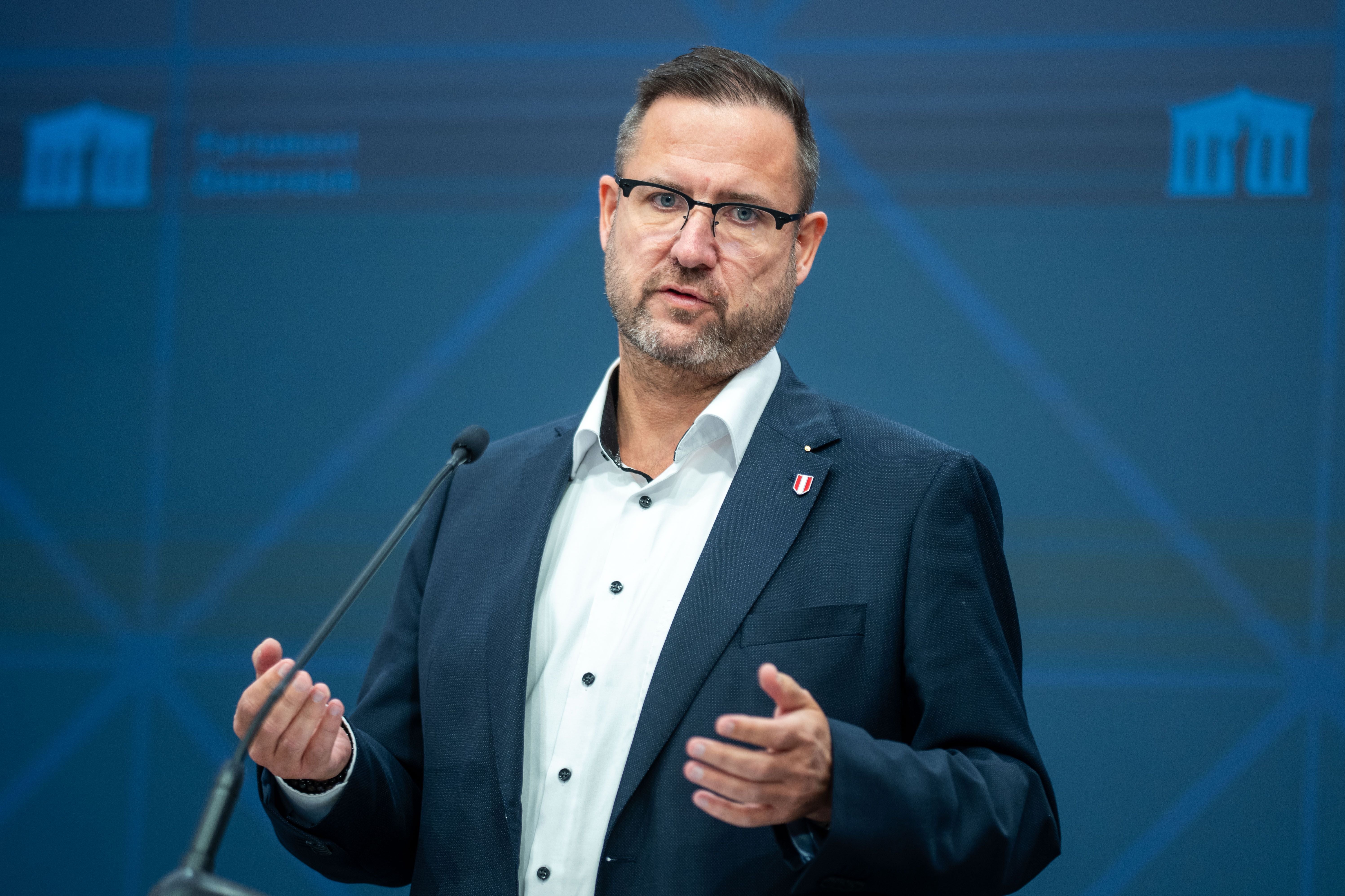 Ein Mann hält eine Rede am Rednerpult vor blauem Hintergrund im Parlament in Wien.