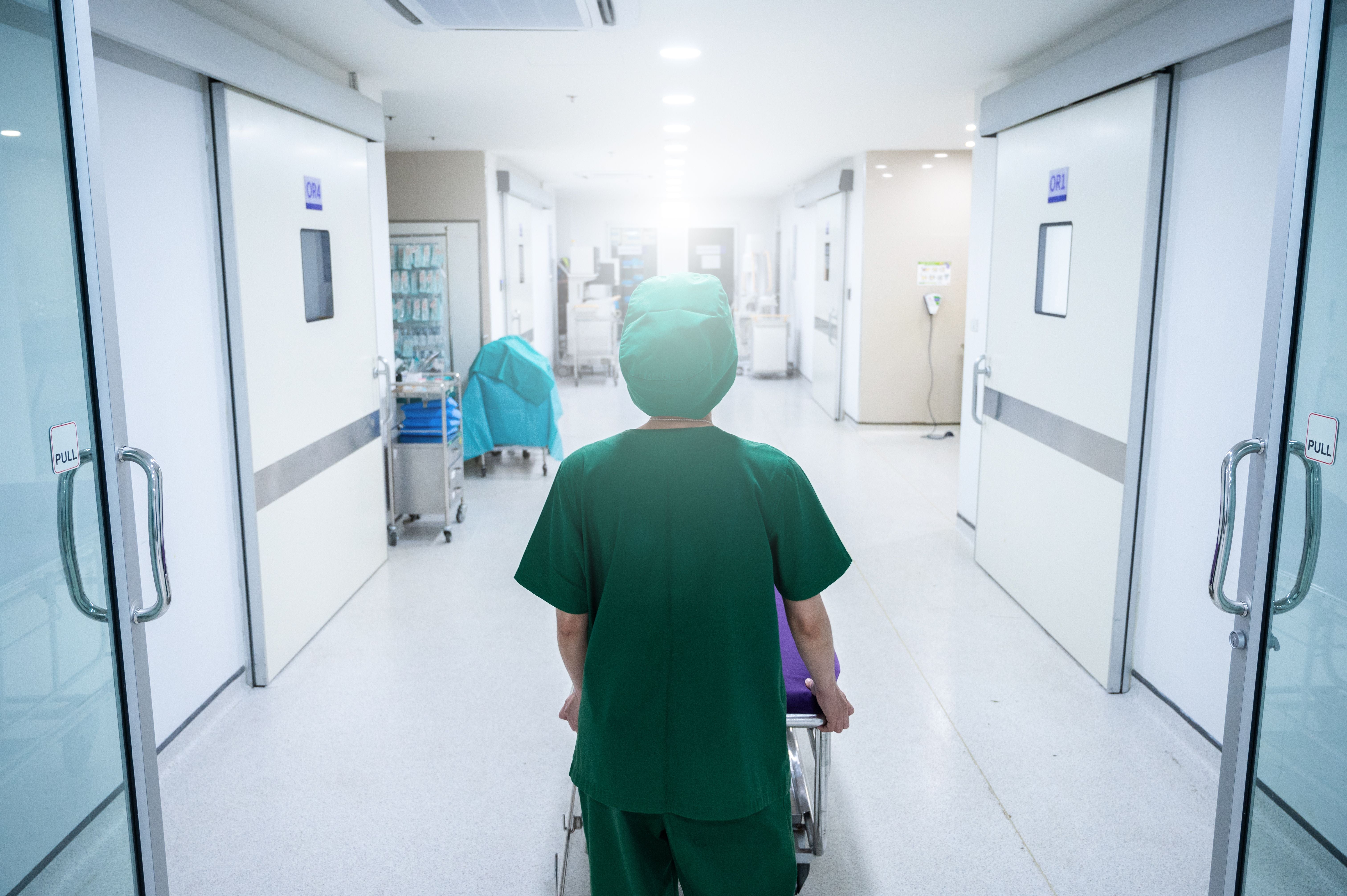 Eine Person in OP-Kleidung schiebt eine Trage durch einen hellen Krankenhausflur.