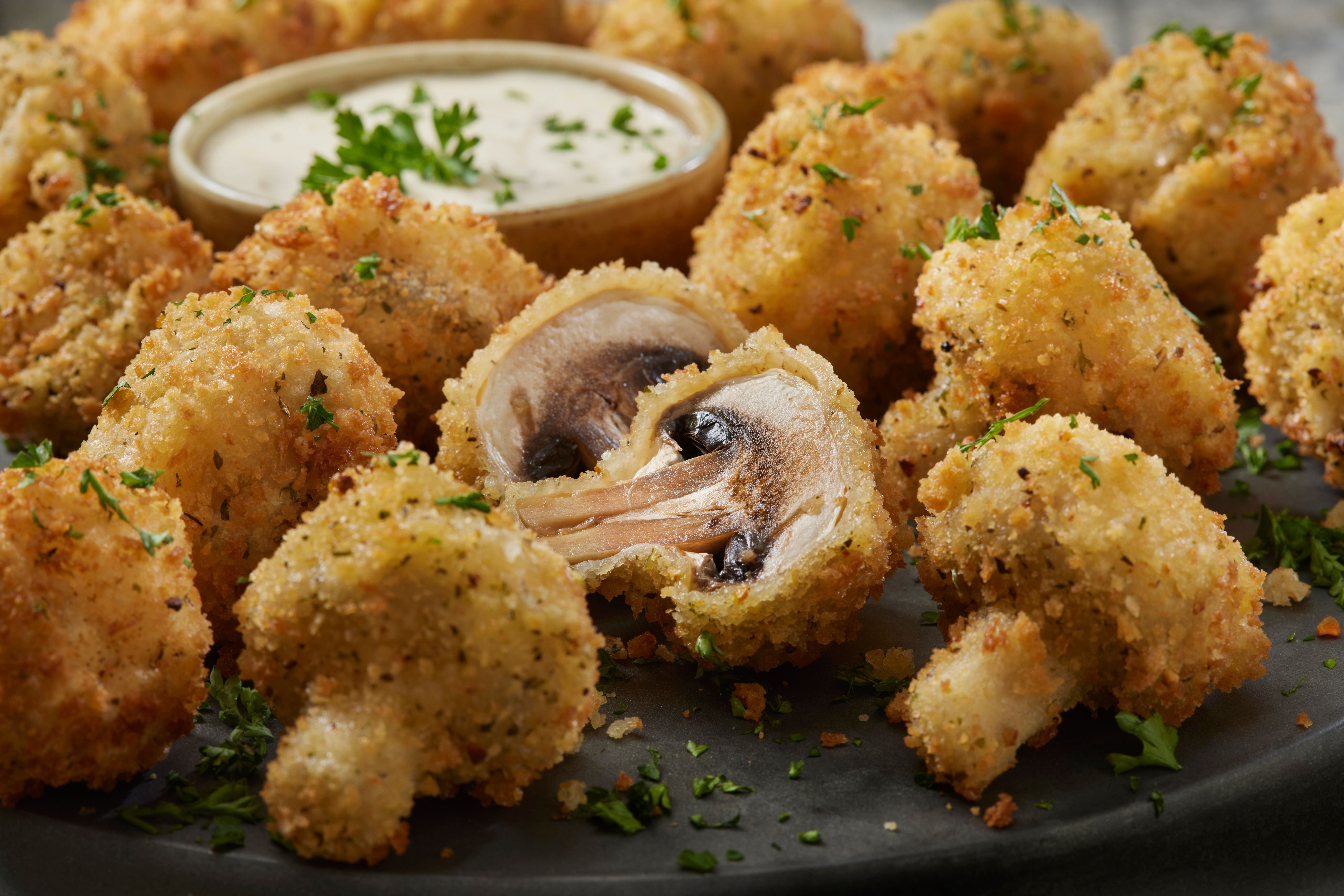 Panierte, frittierte Champignons mit Kräutern, dazu cremiger Ranch-Dip im Hintergrund.