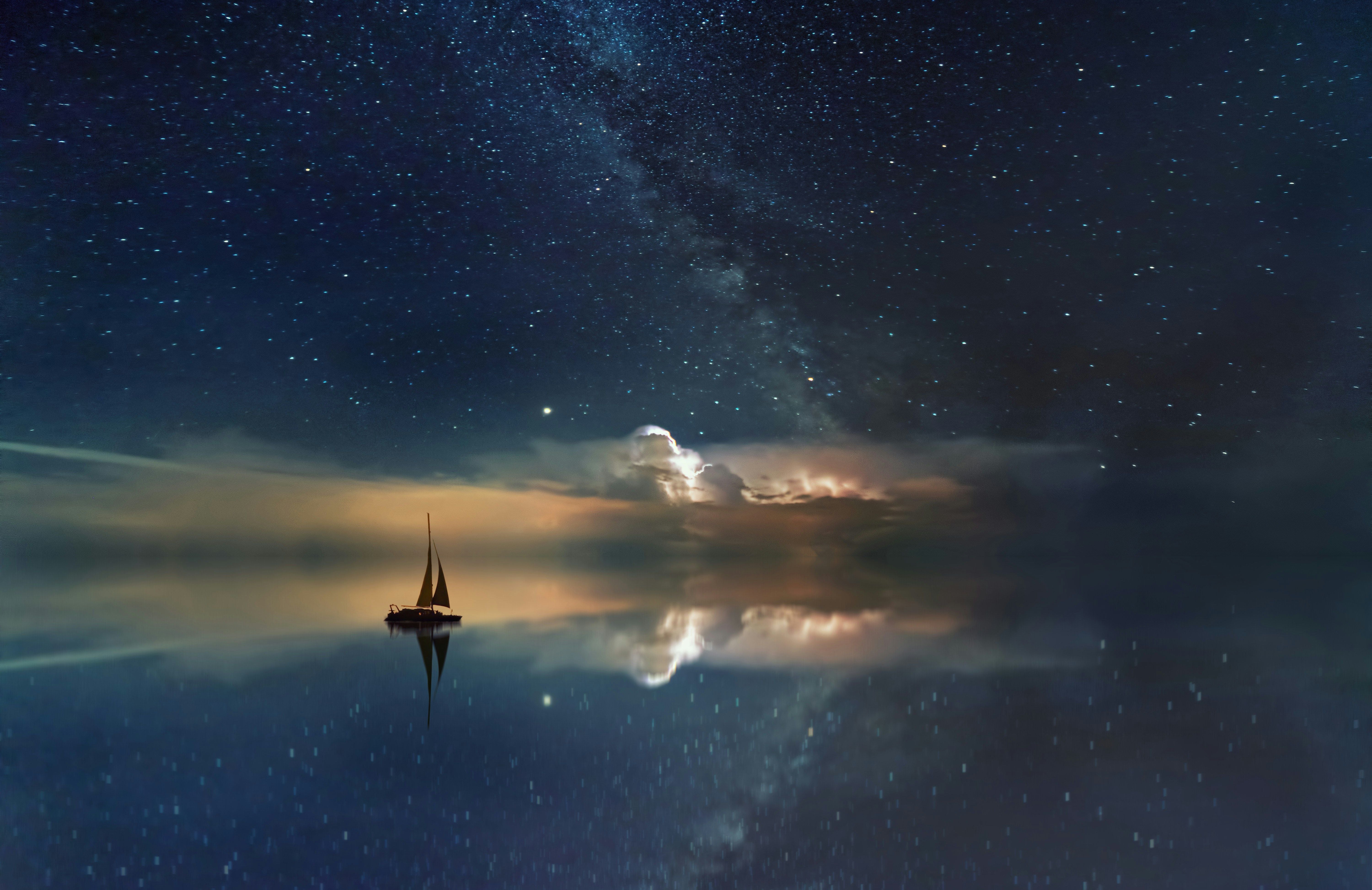 Segelboot auf ruhigem Wasser mit sternenklarem Nachthimmel und leuchtenden Wolken.