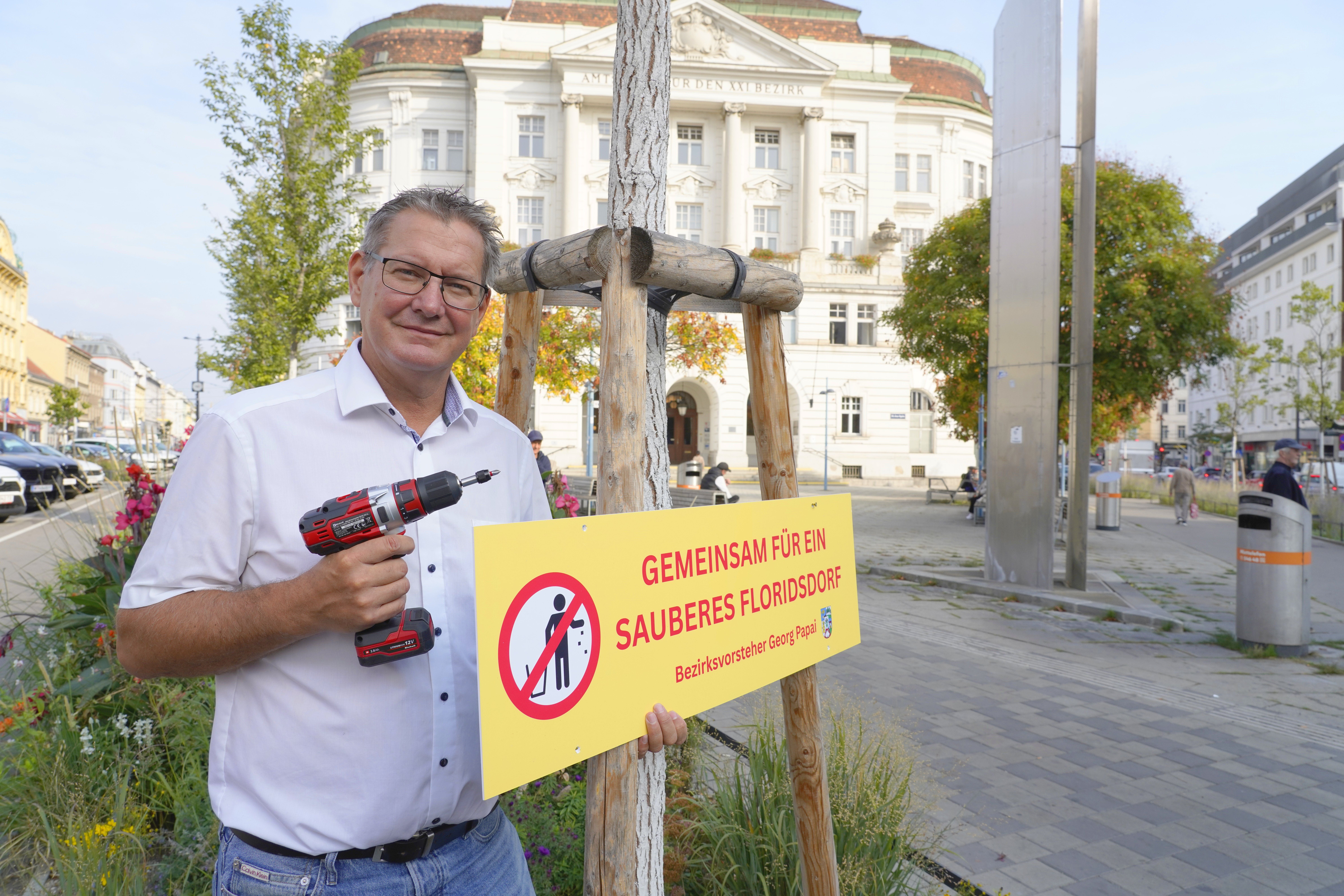 Ein Mann befestigt ein Schild gegen Verschmutzung an einem Baum in einer Stadtstraße.