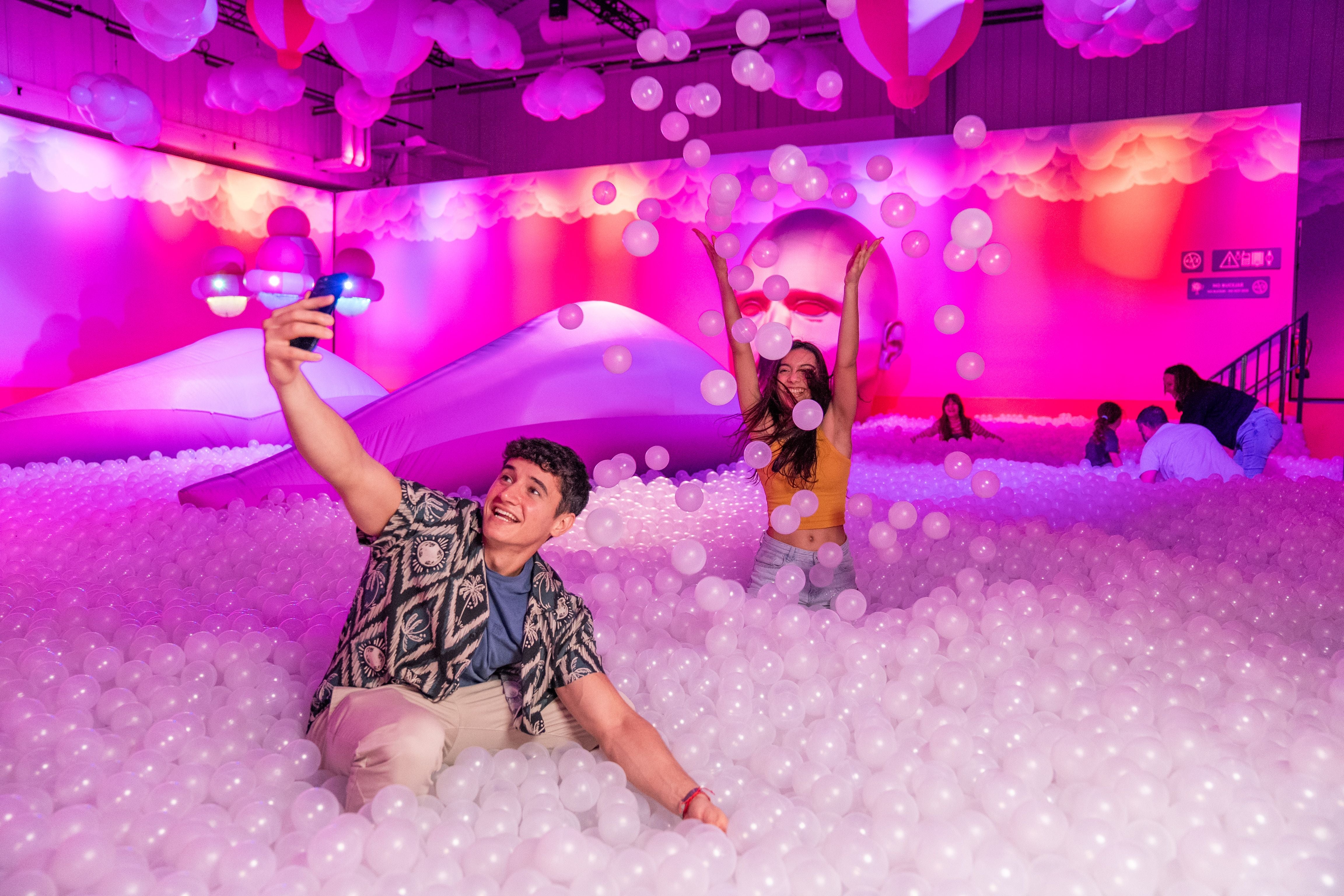 Junge Leute machen Selfies und spielen in einem bunten Bällebad mit Ballons bei Bubble Planet.