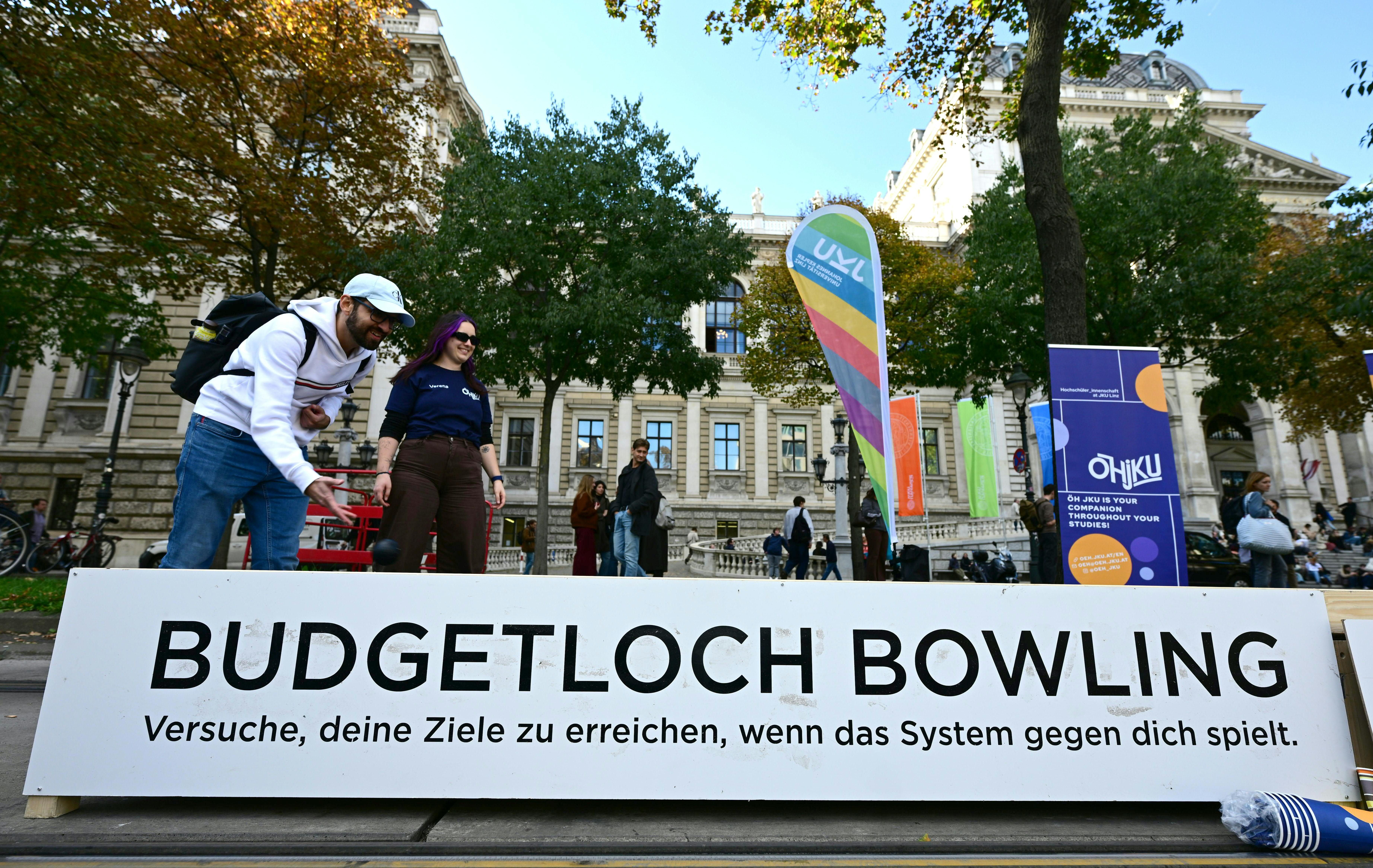 Zwei Personen spielen „Budgetloch Bowling“ bei einer Kundgebung gegen Uni-Einsparungen in Wien.