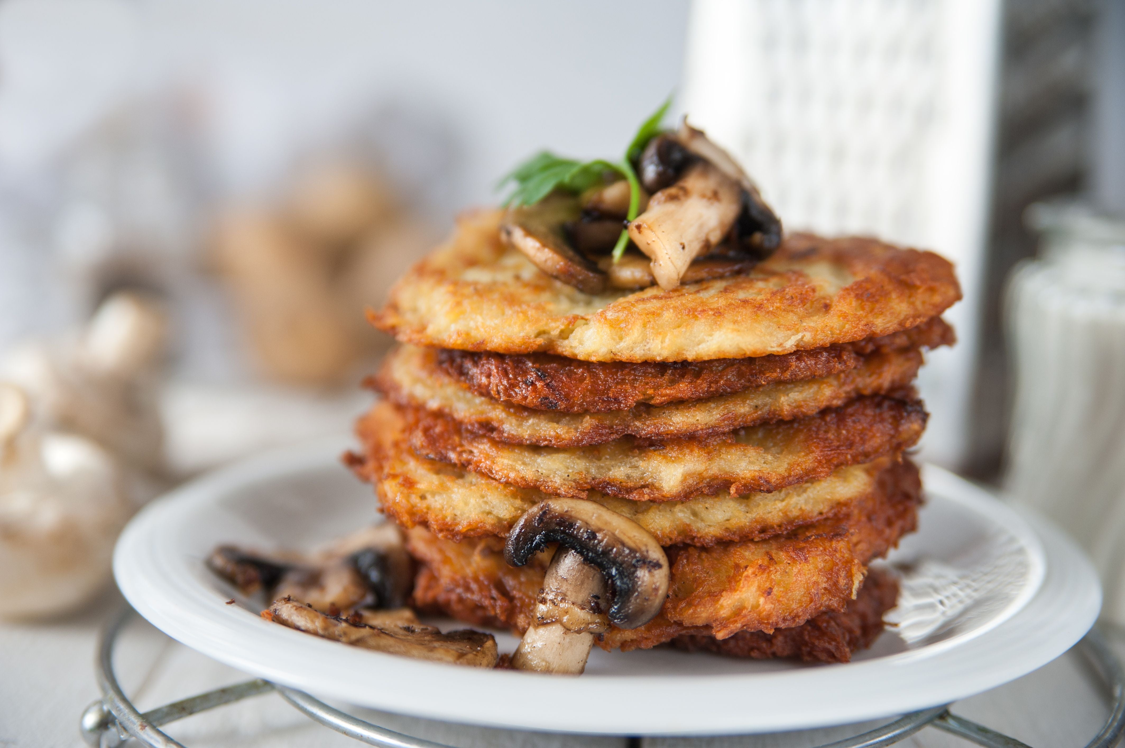Knusprige Kartoffelpuffer mit gebratenen Champignons auf einem weißen Teller.