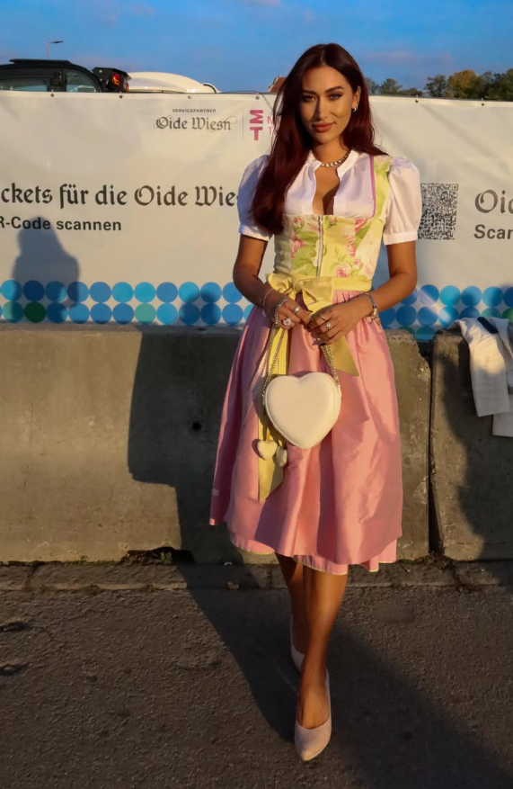 Eine Frau trägt ein Dirndl mit rechts gebundener Schleife und hält eine herzförmige Tasche.