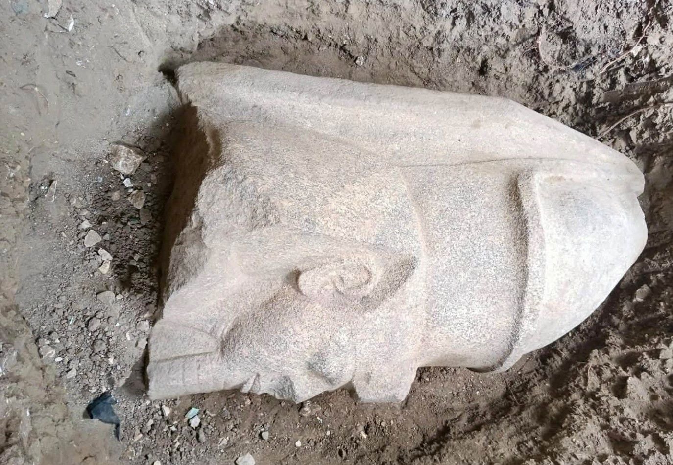 Steinerner Kopf einer Ramses-II.-Statue halb im Sand vergraben.