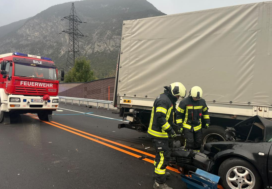 Feuerwehr und Einsatzkräfte an Unfallstelle mit Lkw und zerstörtem Auto in Silz, Tirol.