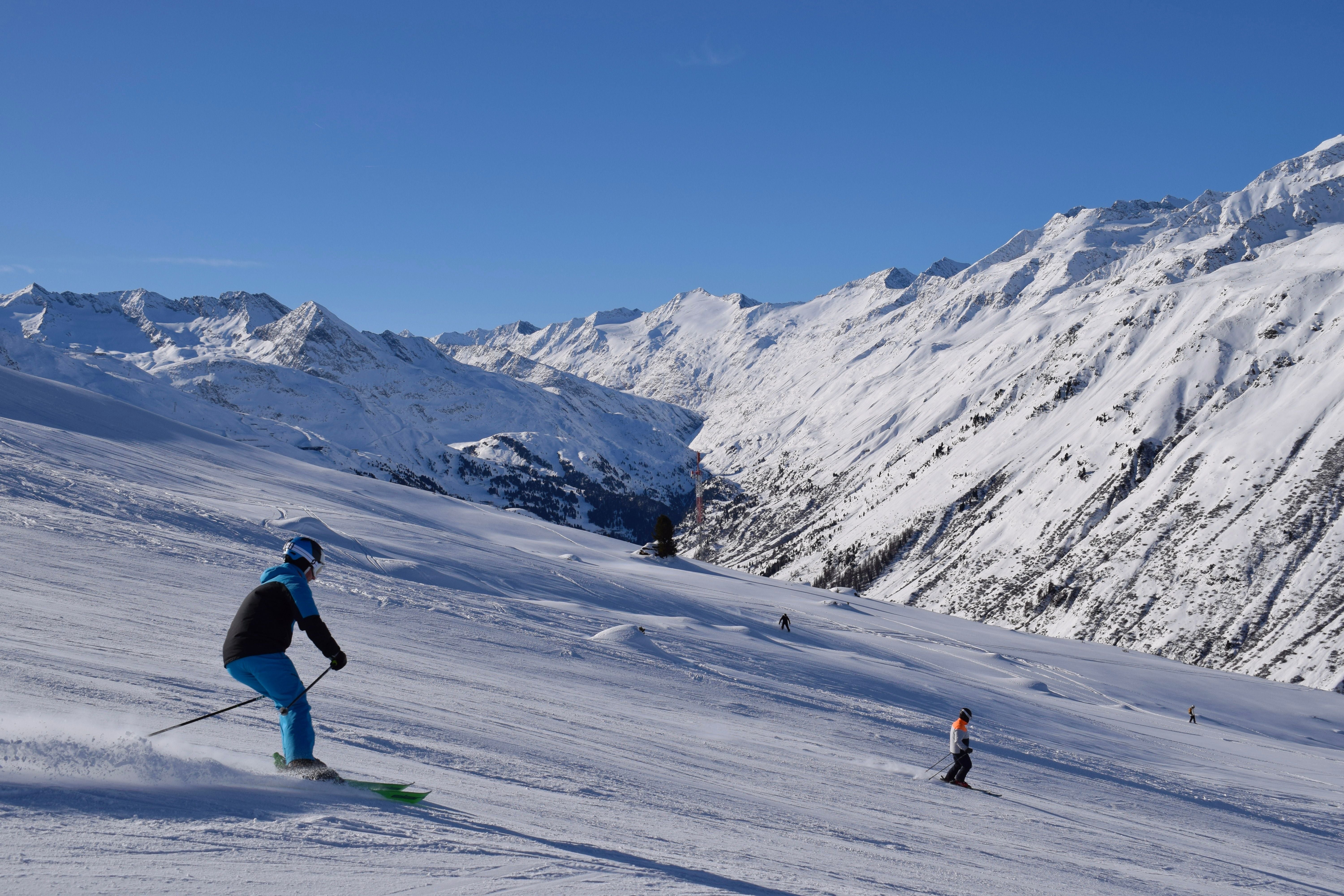 Skifahrer auf einer sonnigen Piste mit verschneiten Alpen im Hintergrund in Hochgurgl, Tirol.