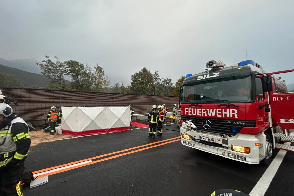 Feuerwehr und Einsatzkräfte sichern Unfallstelle mit Absperrzelt und Feuerwehrauto auf Straße.
