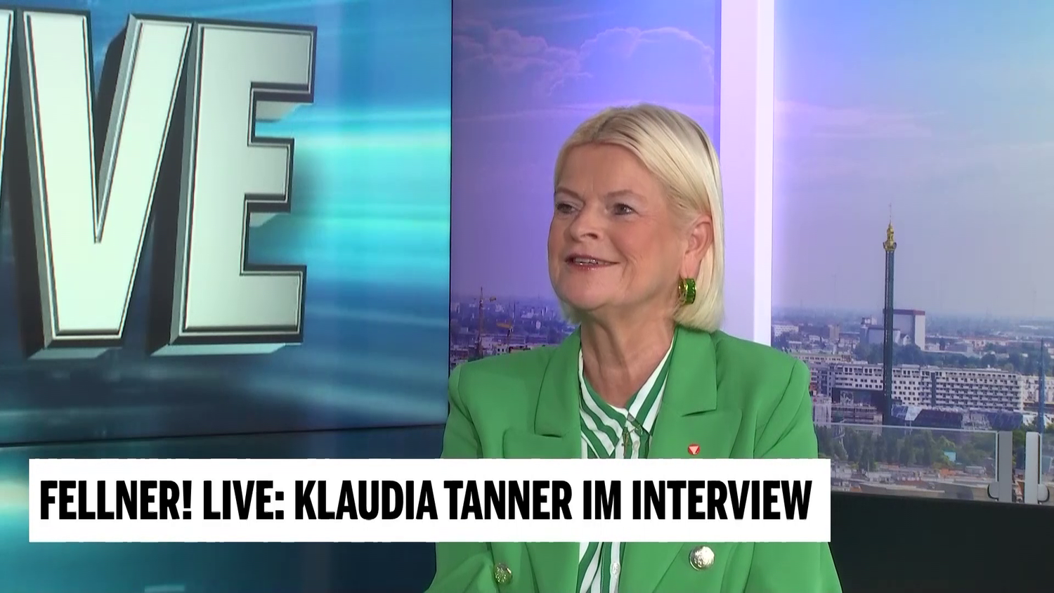 Eine Frau im grünen Blazer wird in einer Fernsehsendung interviewt.