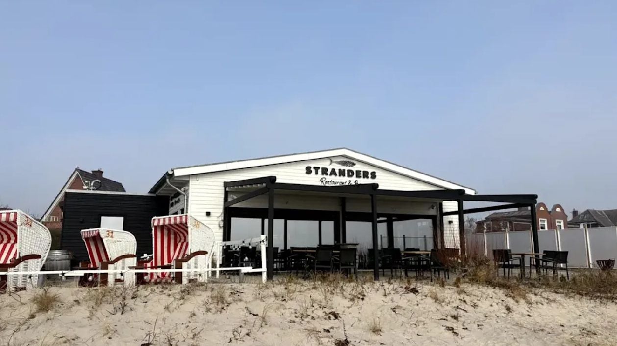 Weißes Strandcafé „Stranders“ mit Strandkörben und Terrasse am Sandstrand.