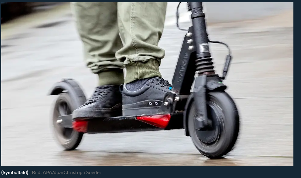 Person fährt mit einem E-Scooter auf nasser Straße, Fokus auf Schuhe und Roller.
