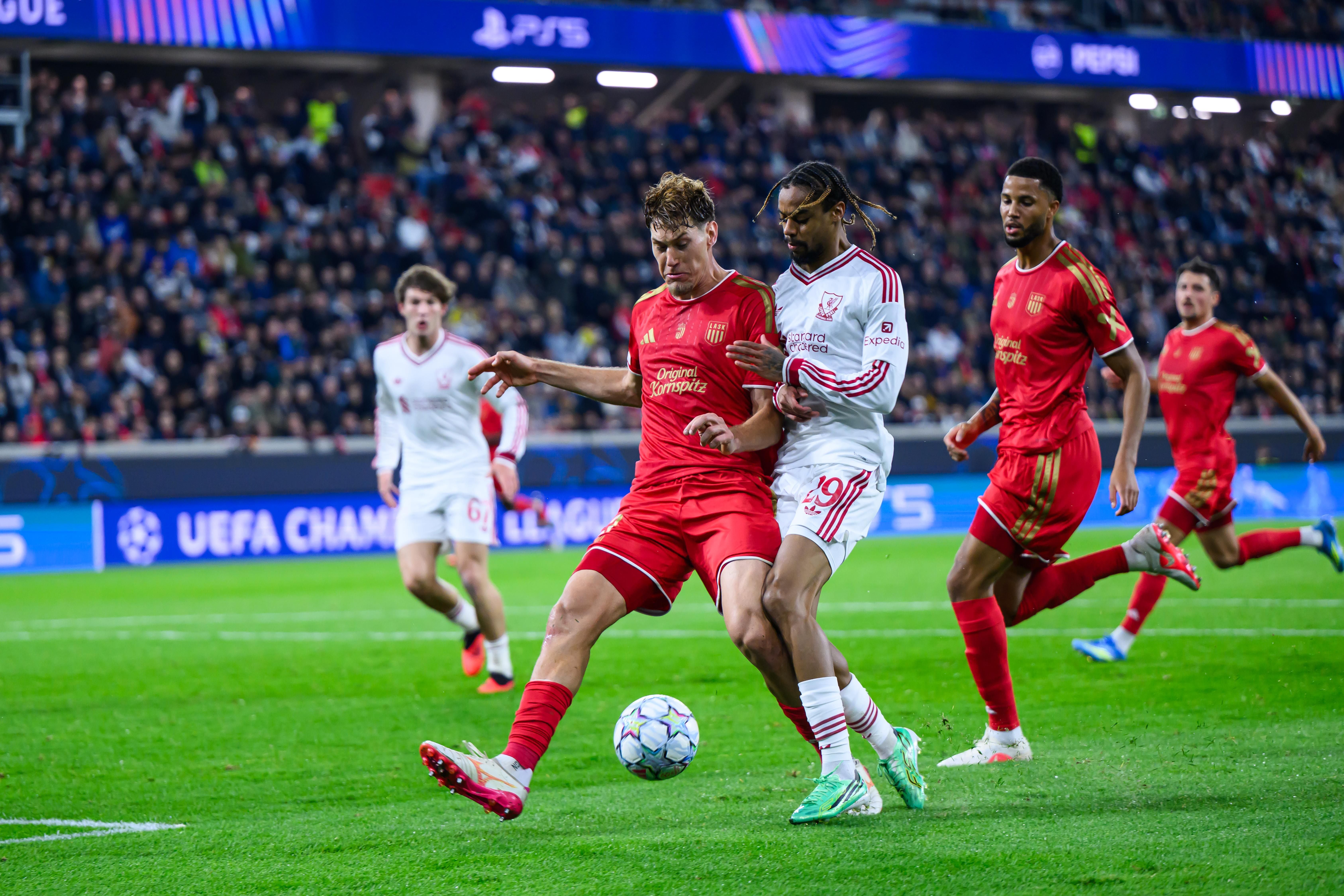 Zwei Fußballspieler kämpfen im Champions-League-Spiel um den Ball, Zuschauer im Hintergrund.