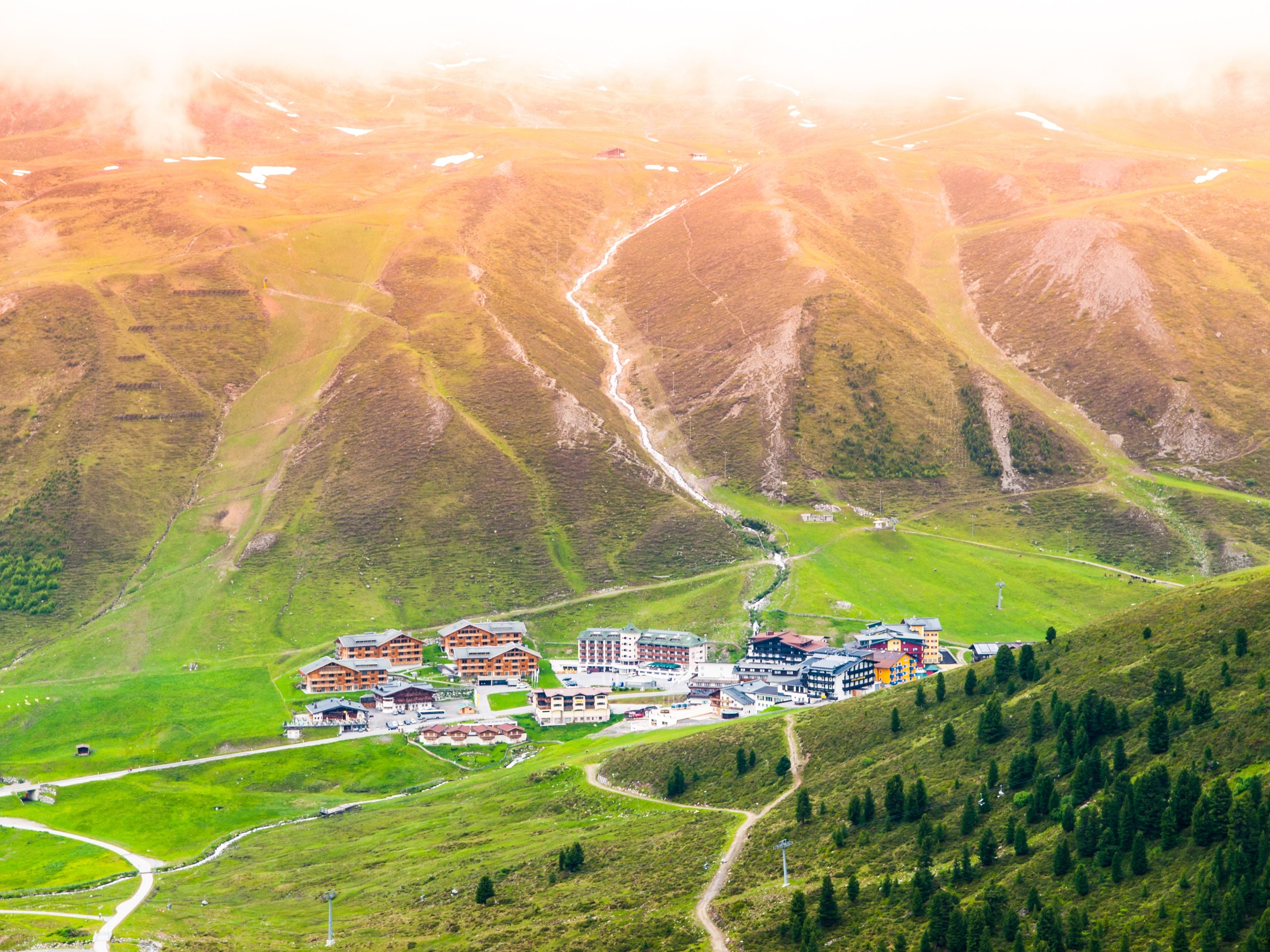 Alpines Skigebiet Kühtai im Sommer mit grünen Hängen und einem kleinen Dorf im Tal.