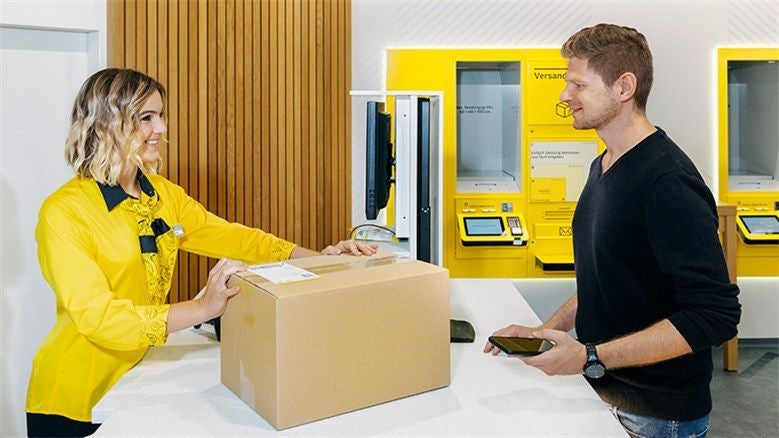 Ein Mann gibt ein Paket bei einer Postmitarbeiterin am Schalter zum Versand ab.