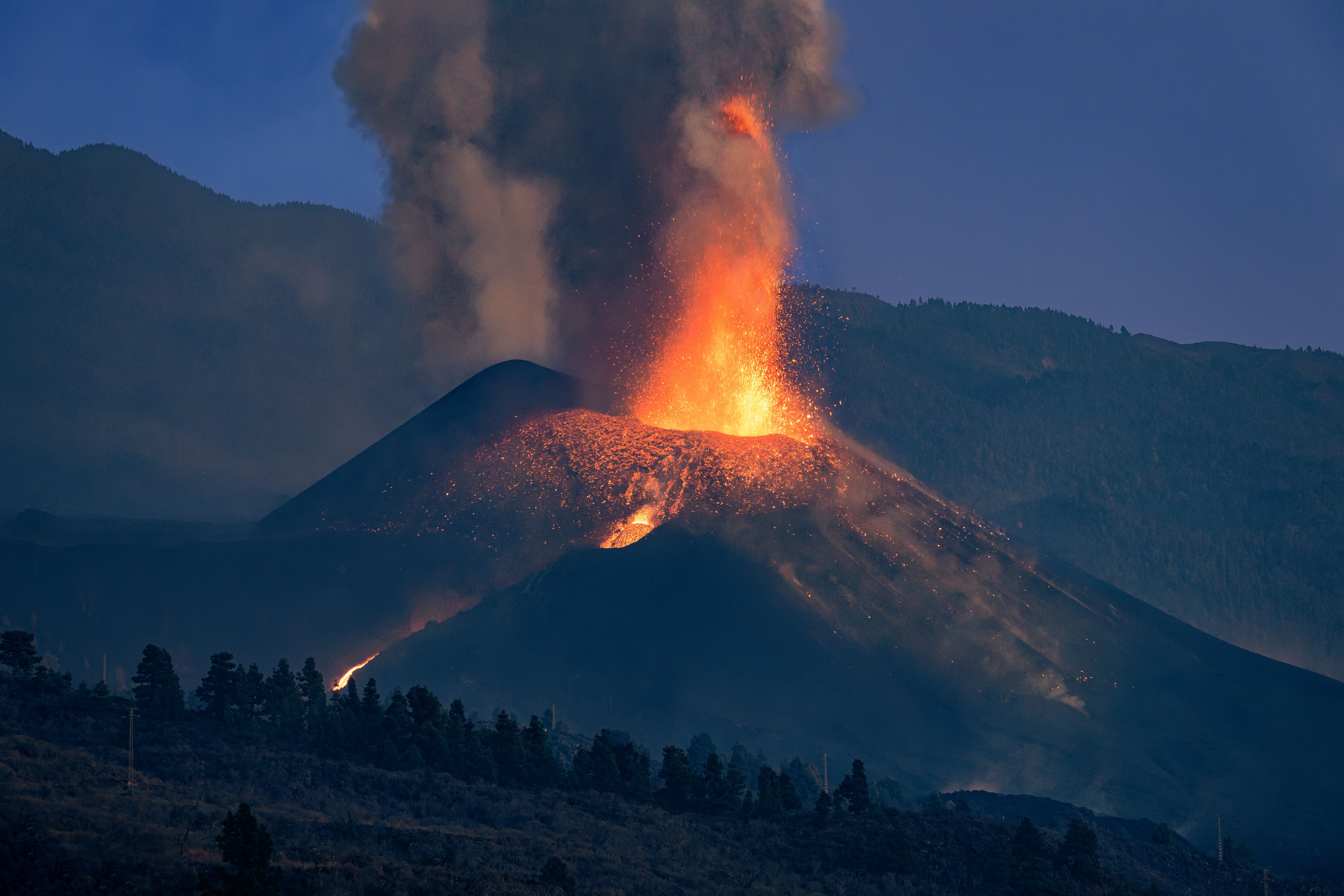 Vulkanausbruch bei Sonnenuntergang mit Lava und Rauch am Cumbre Vieja Vulkan, Berge im Hintergrund.