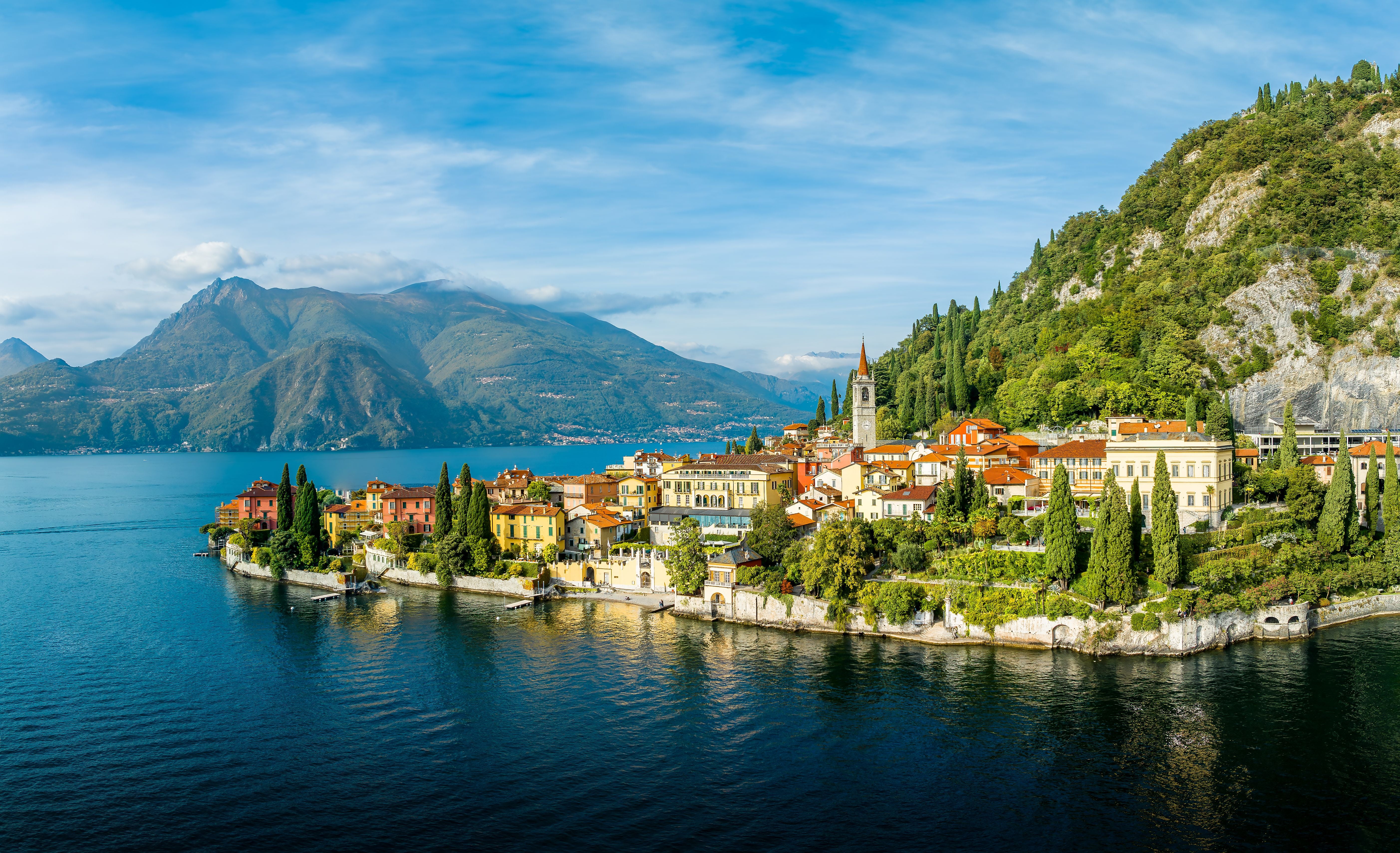Blick auf die bunte Stadt Varenna am Comer See vor bewaldeten Hügeln und Bergen in Italien.