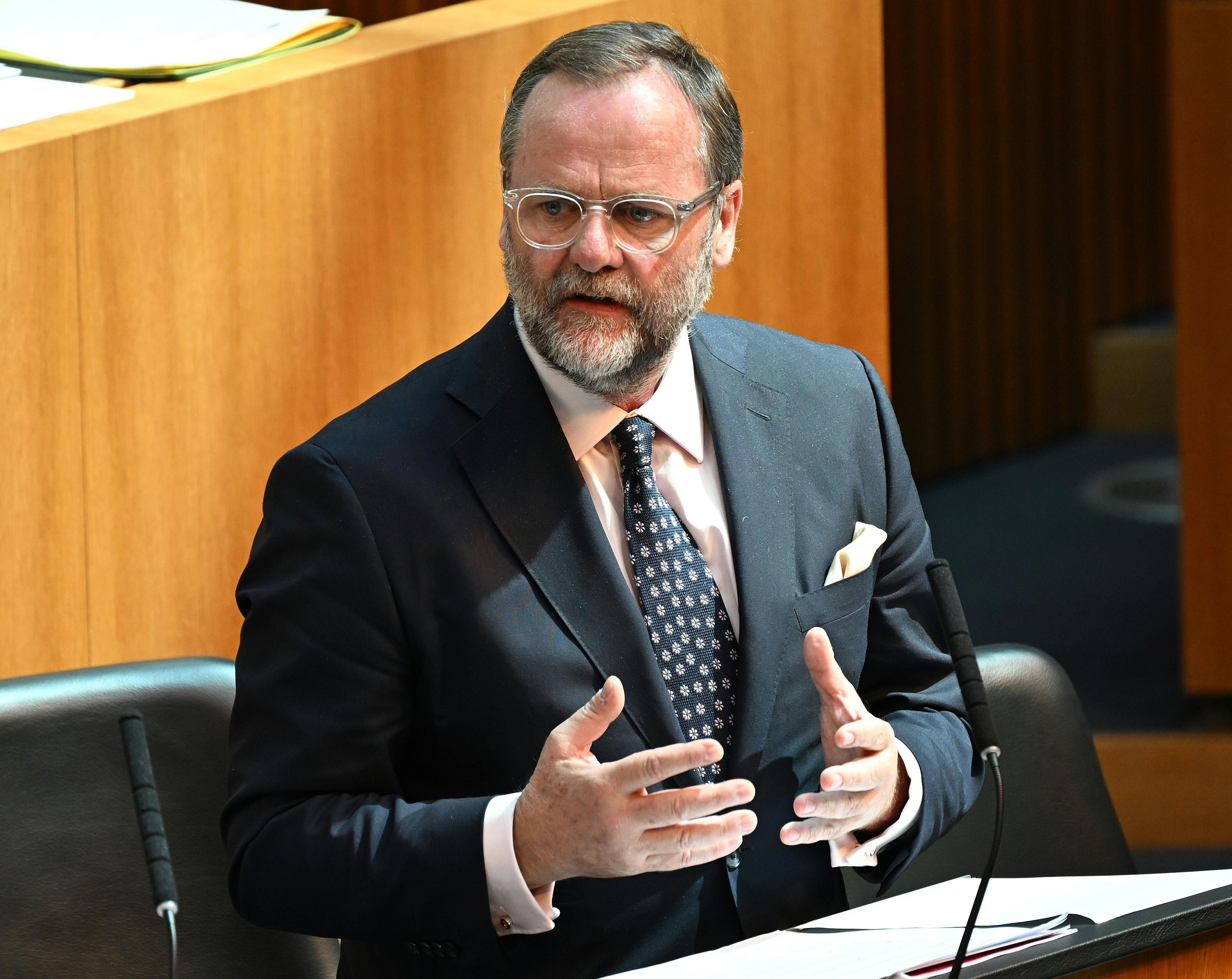 Ein Mann im Anzug spricht während einer Parlamentssitzung an einem Rednerpult.