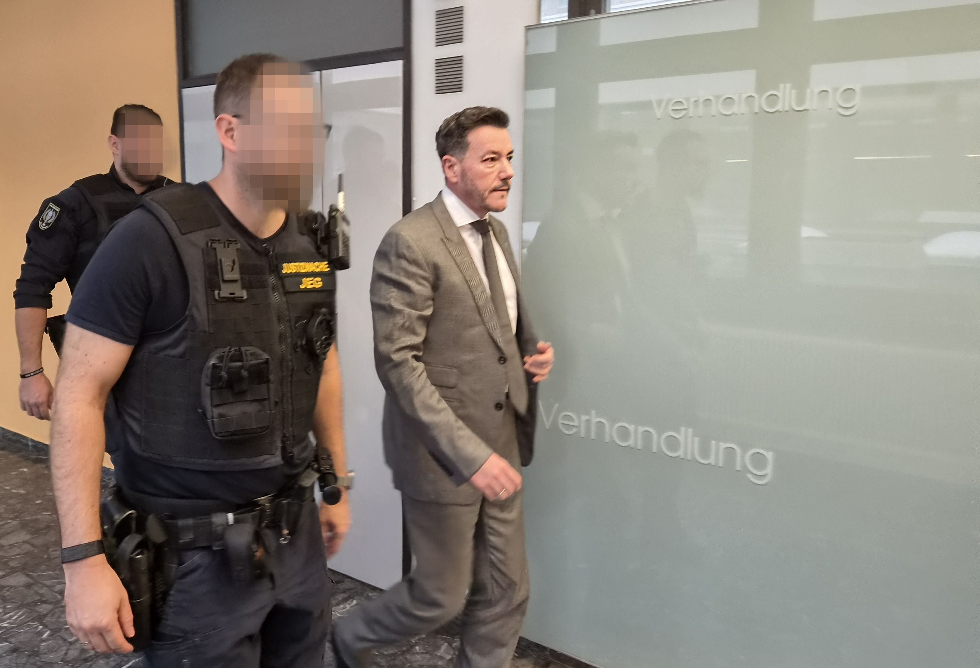 Ein Mann im grauen Anzug verlässt mit Justizbeamten einen Raum im Landesgericht Innsbruck.