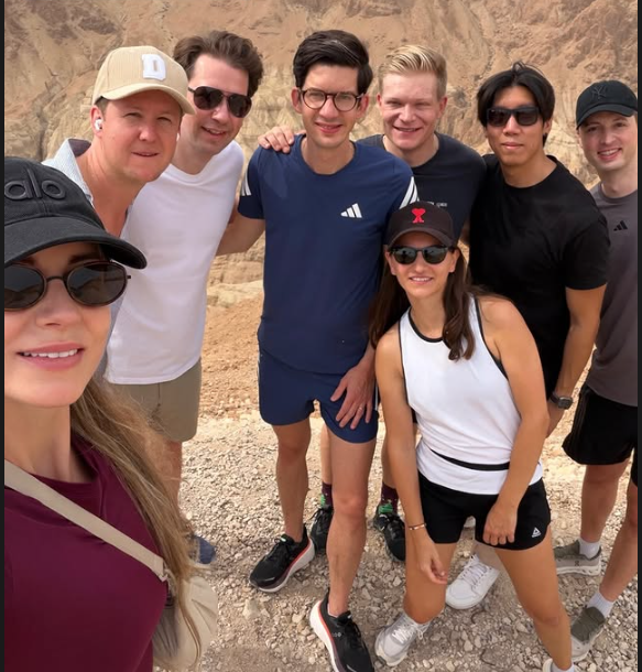 Eine Gruppe junger Menschen posiert lächelnd in sportlicher Kleidung vor einer Felslandschaft.