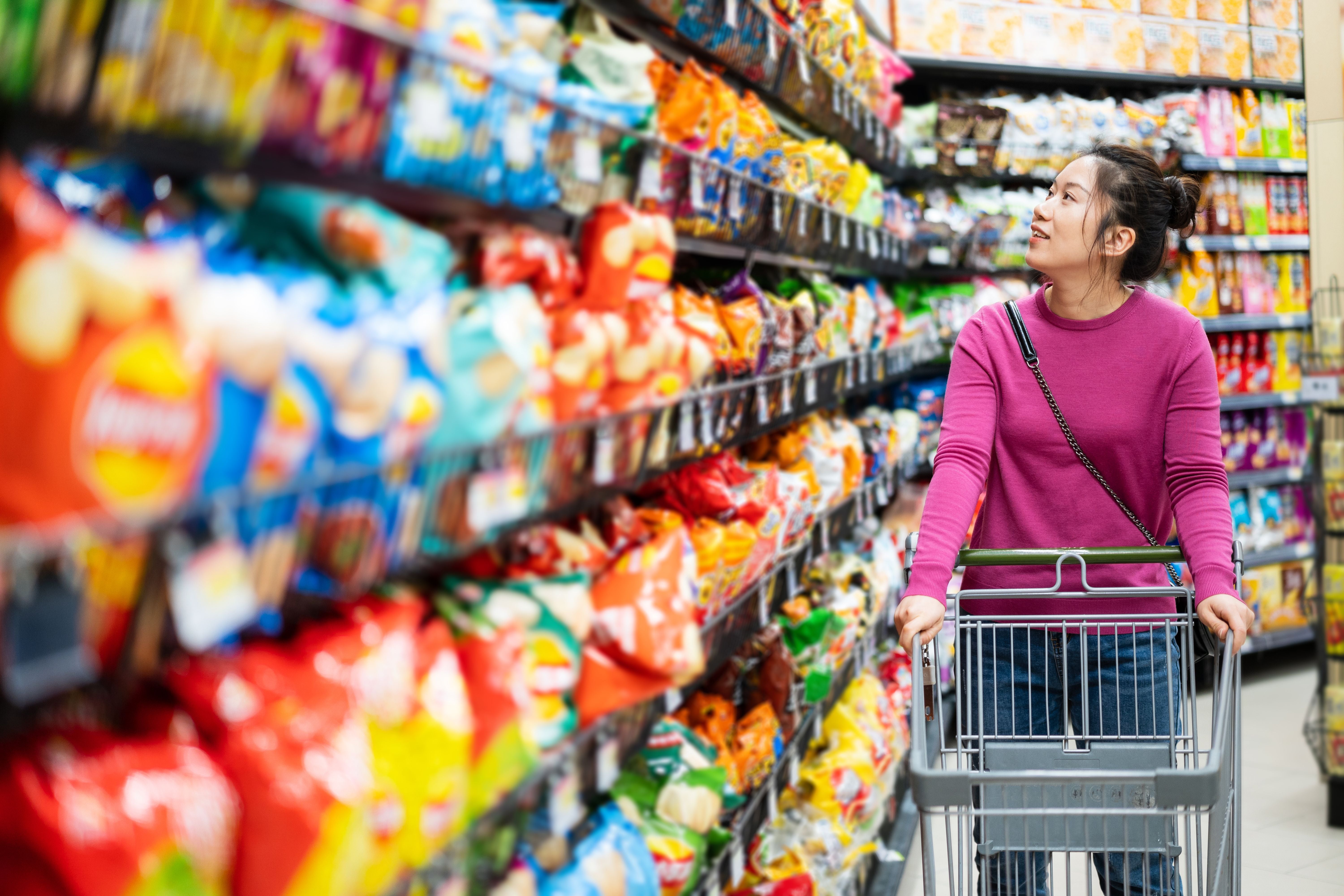 Frau mit Einkaufswagen betrachtet Snackregale im Supermarkt.