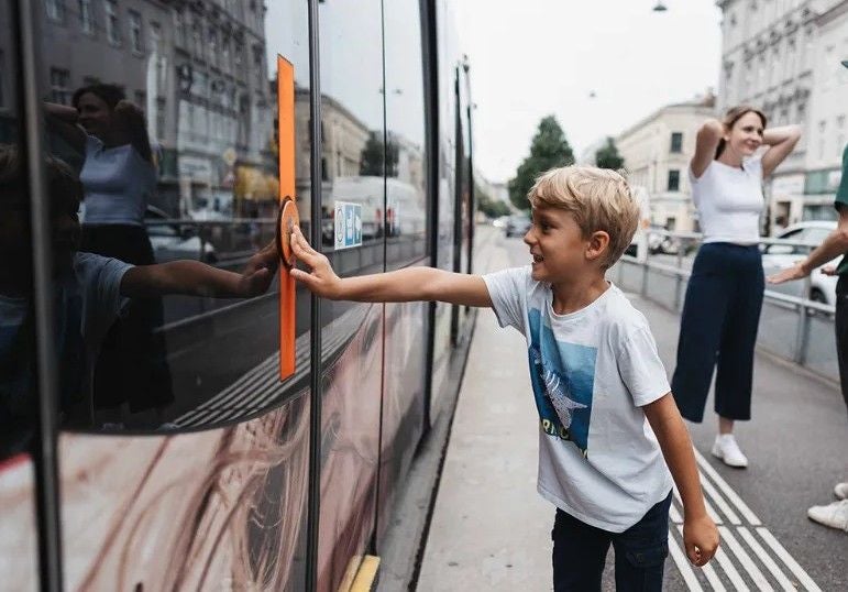 Junge drückt den Taster an einer Straßenbahn, im Hintergrund stehen zwei Erwachsene.
