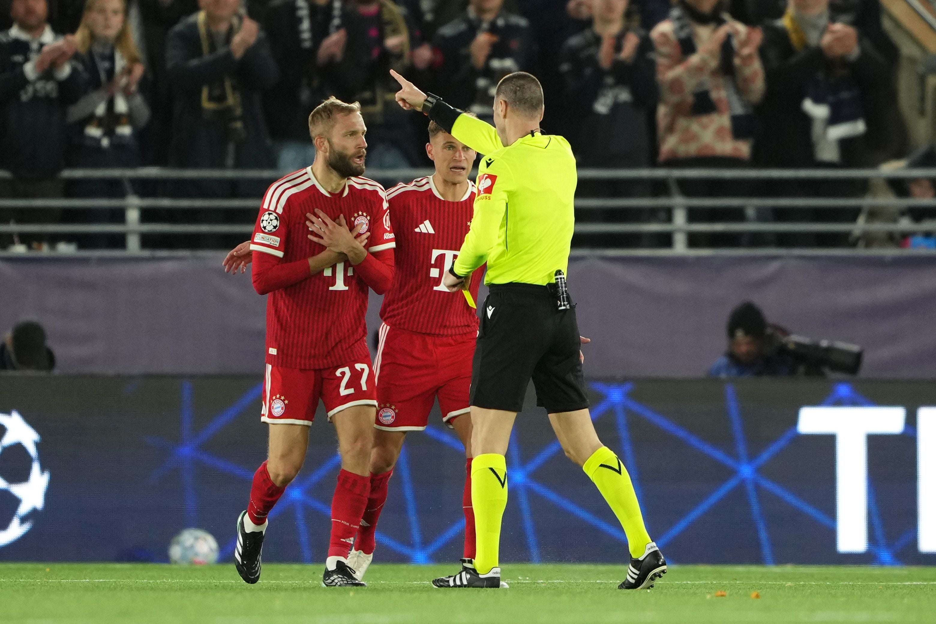 Zwei Bayern-Spieler diskutieren auf dem Spielfeld mit einem Schiedsrichter in gelber Kleidung.