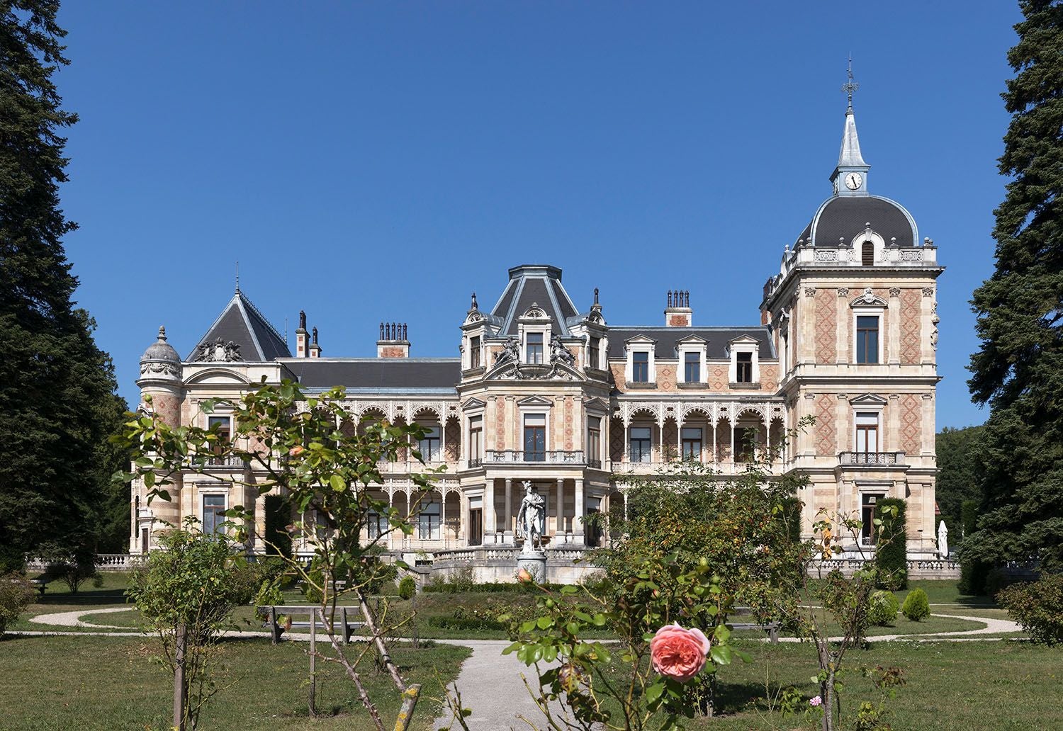 Prunkvolle Hermesvilla in Wien, umgeben von Garten und blühenden Rosen im Vordergrund.