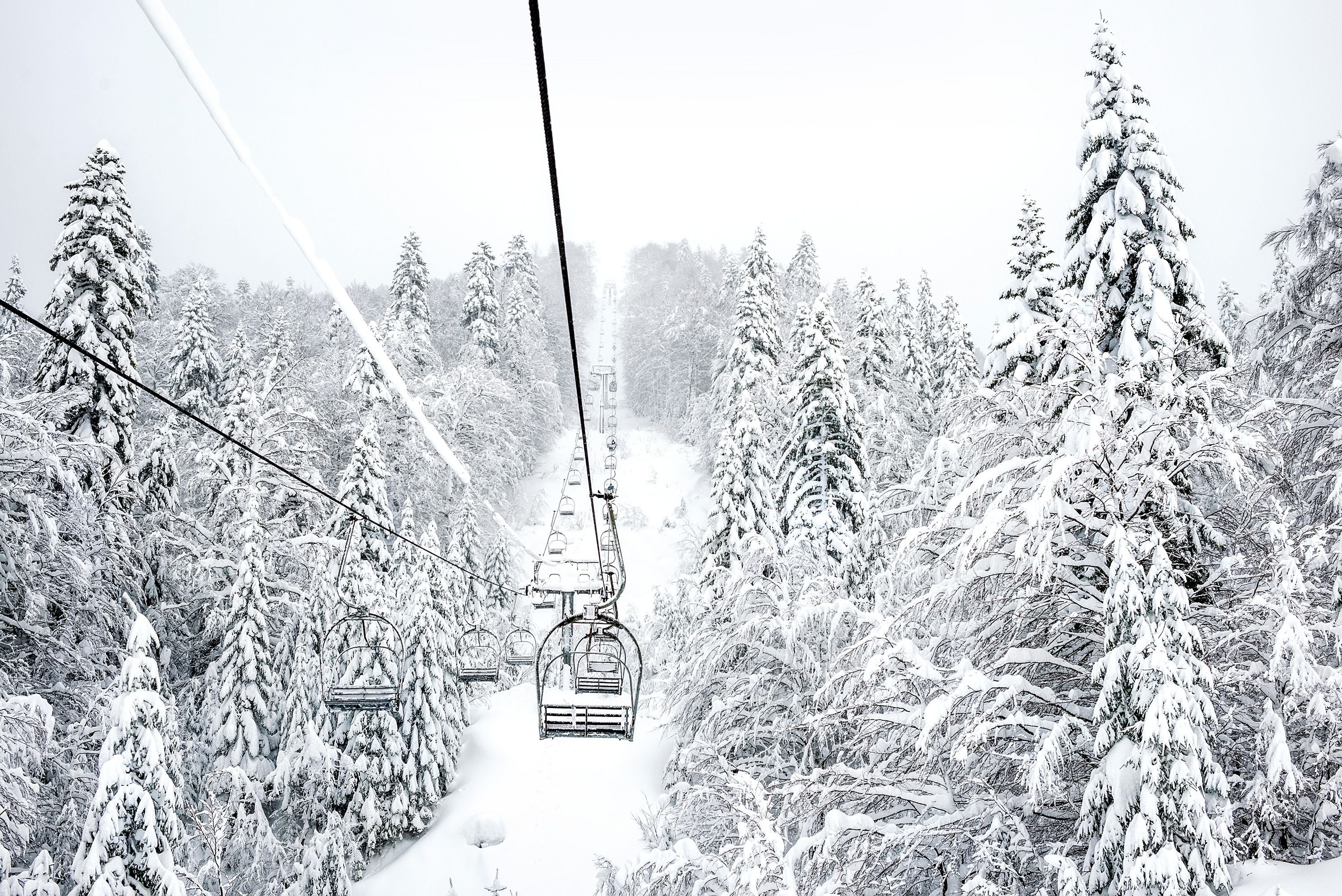 Leerer Skilift über schneebedecktem Nadelwald im Winter, alles dick mit Schnee bedeckt.