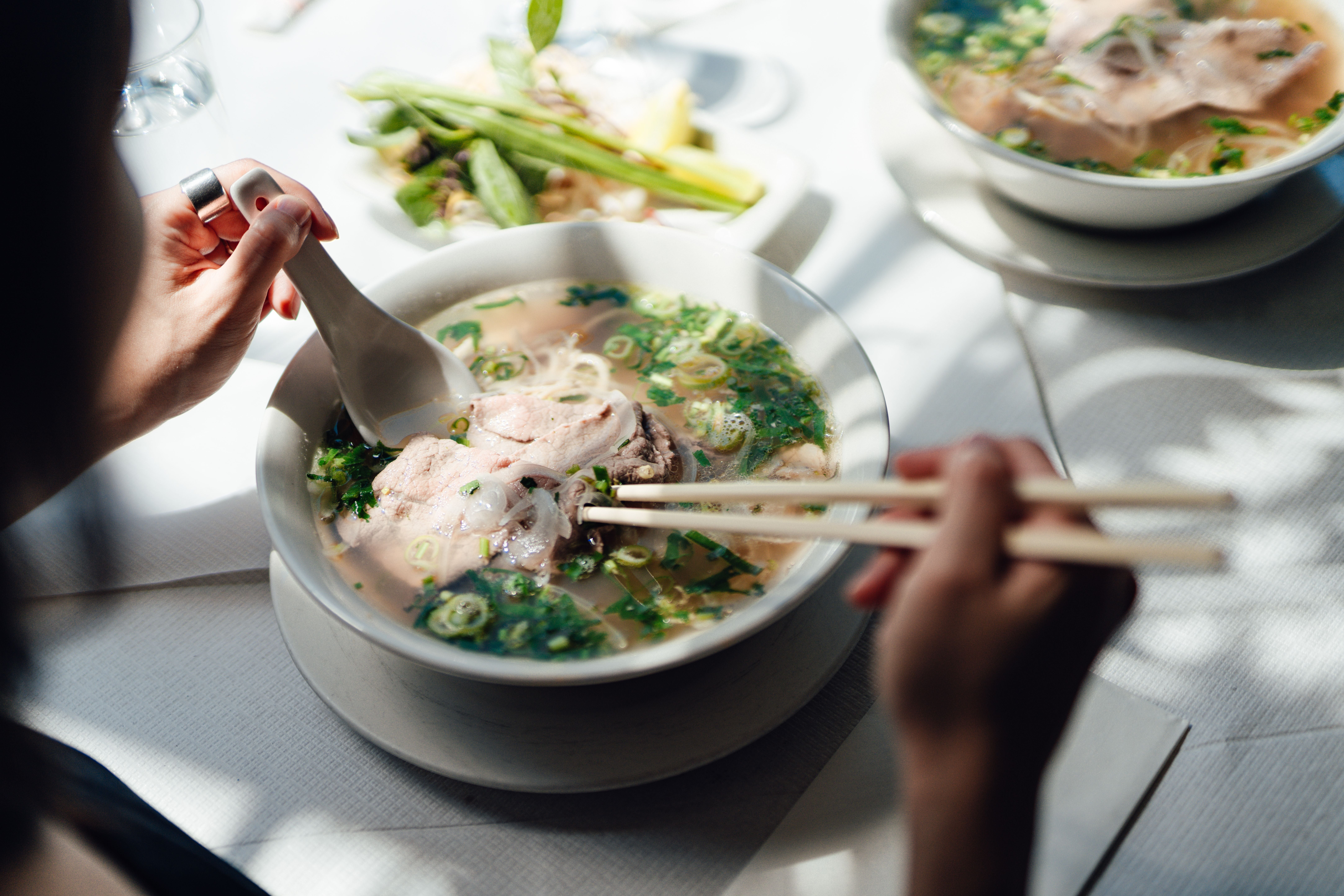 Frau isst Pho-Suppe mit Stäbchen und Löffel in einem Restaurant.