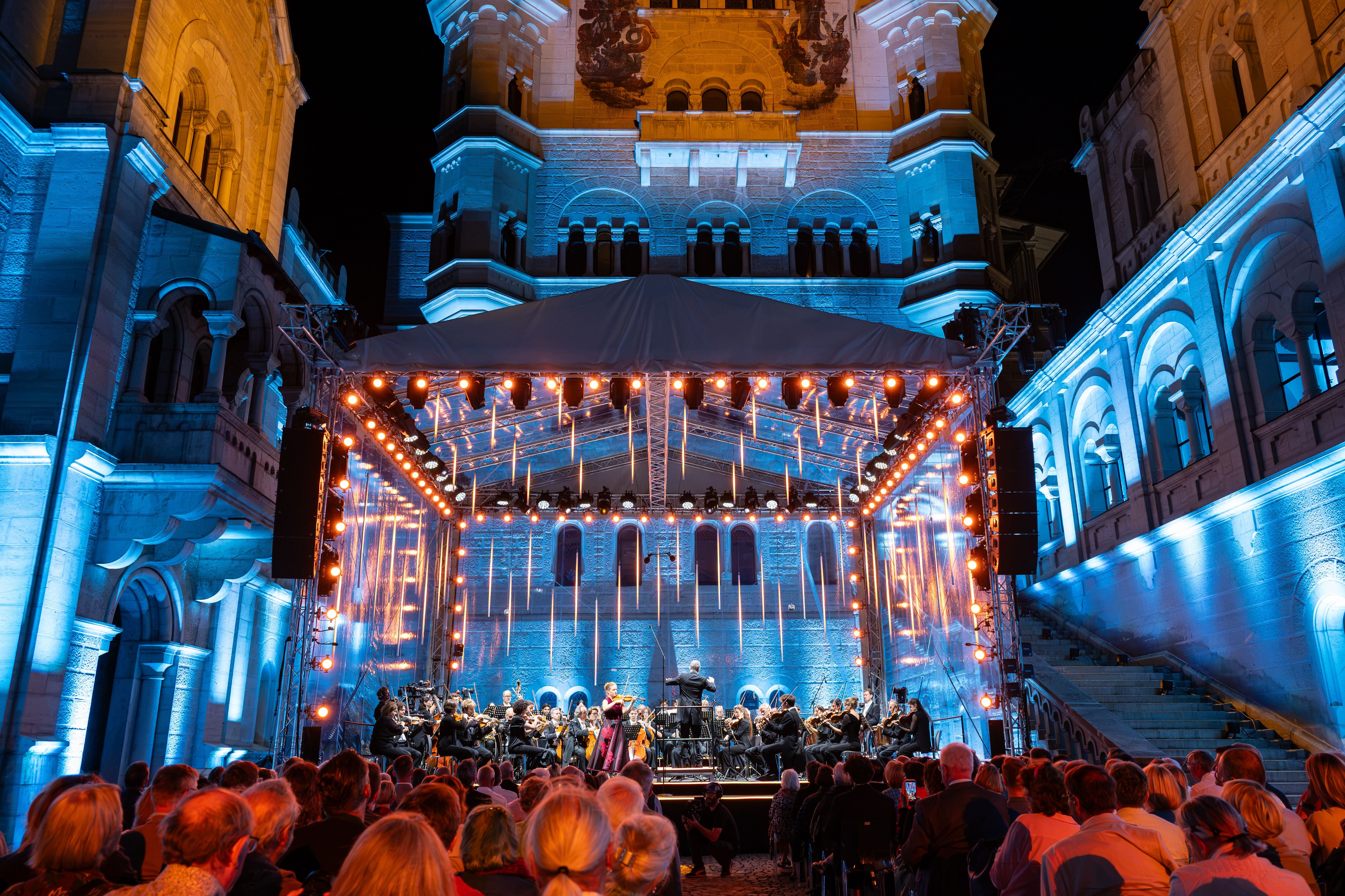 Open-Air-Konzert vor Schloss Neuschwanstein, das in blauem Licht angestrahlt wird.