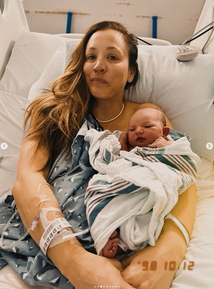 Frau liegt im Krankenhausbett und hält ein neugeborenes Baby im Arm.
